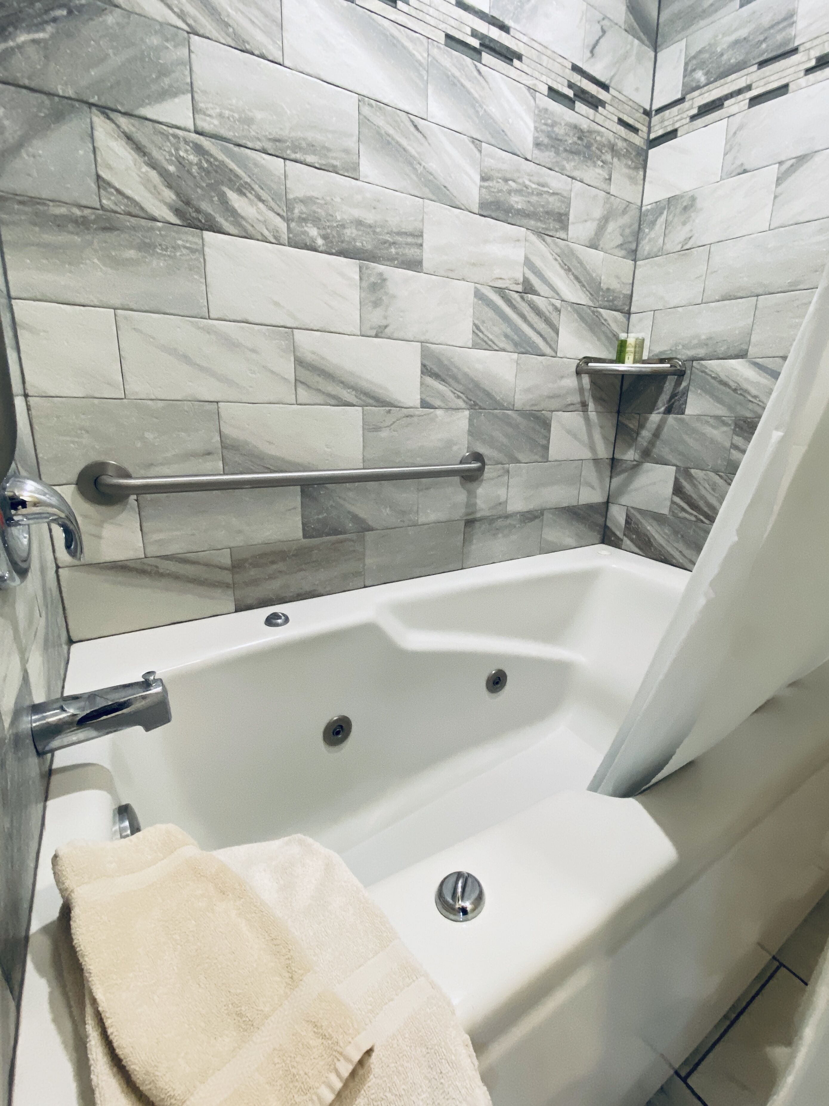 Ein Badezimmer mit einer weißen Badewanne, einer Haltestange und einem Handtuch.