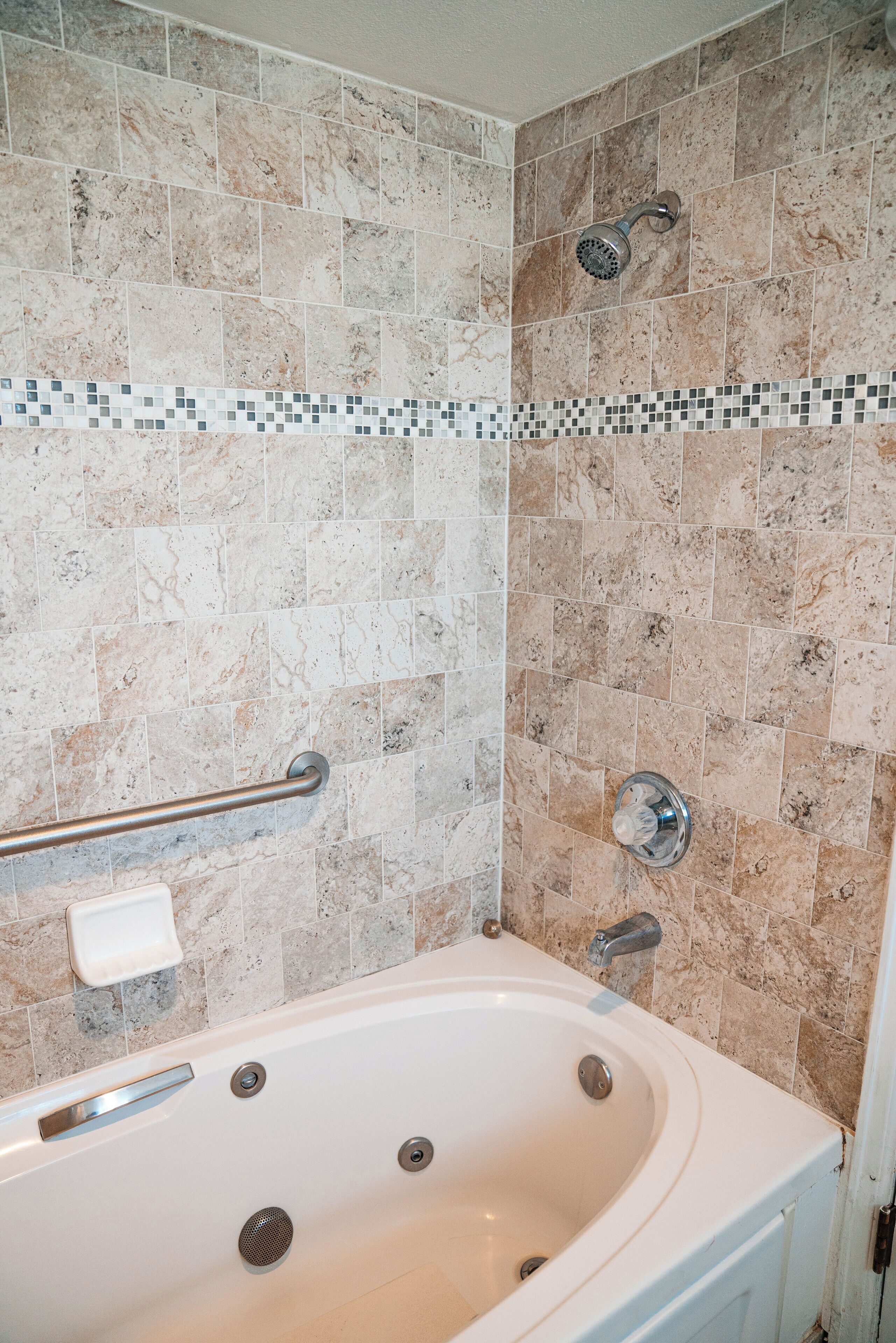 A bathroom with a bathtub, a showerhead, and a tiled wall with a decorative border.