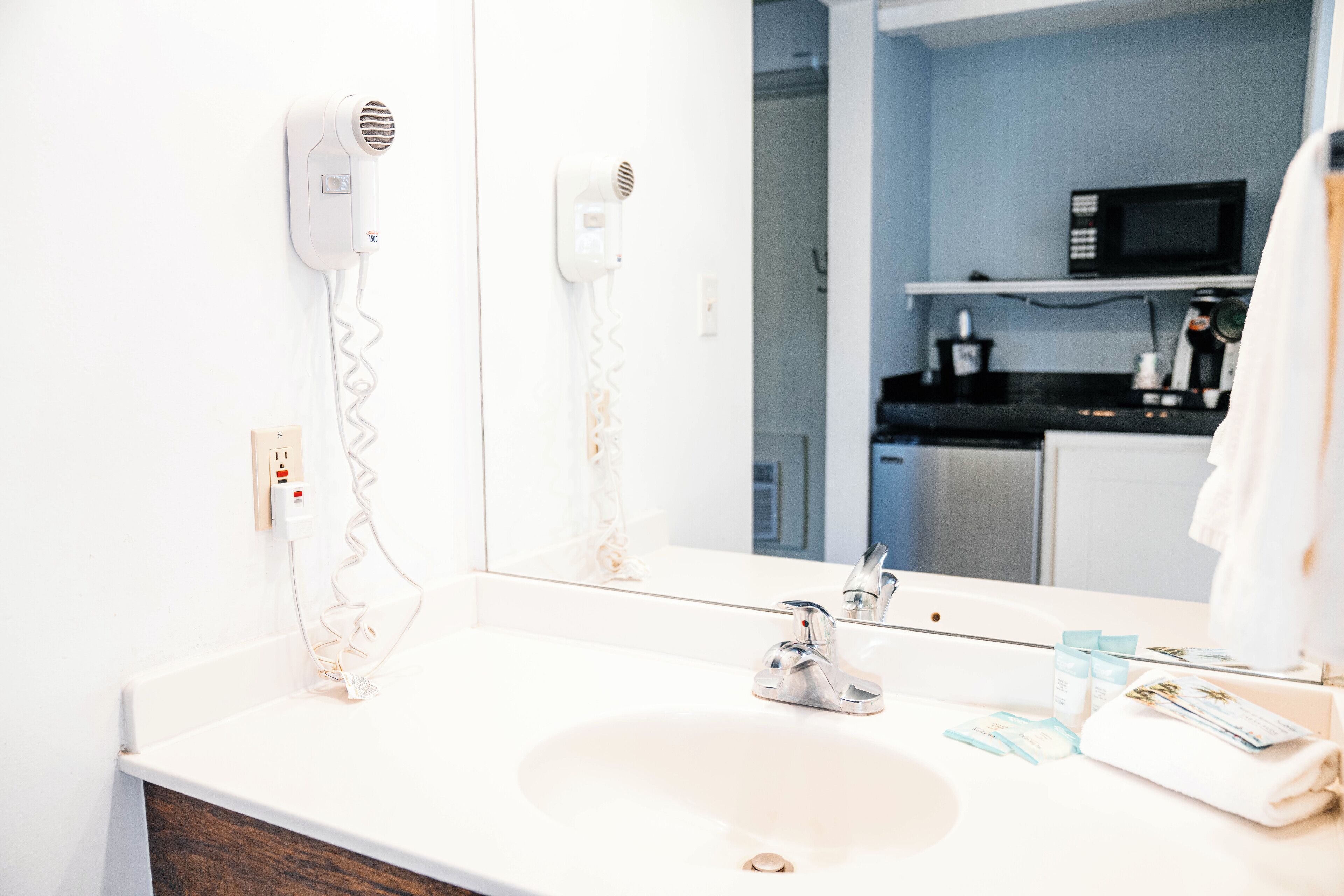 Un baño con un lavabo blanco, un espejo, un secador de pelo y una toalla.
