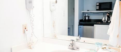 Un baño con un lavabo blanco, un espejo, un secador de pelo y una toalla.