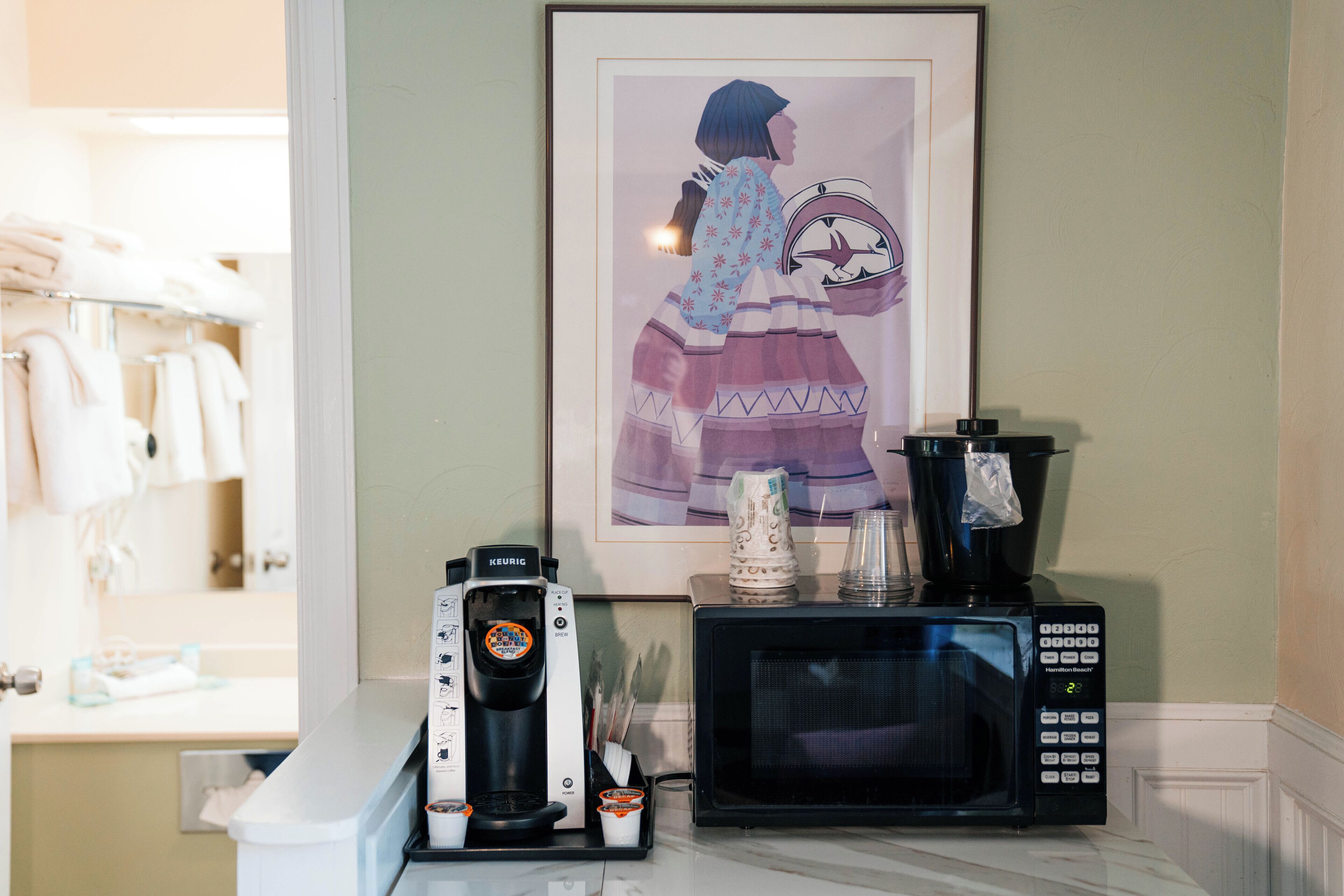 A kitchenette with a Keurig coffee maker, a microwave, and a framed illustration on the wall.