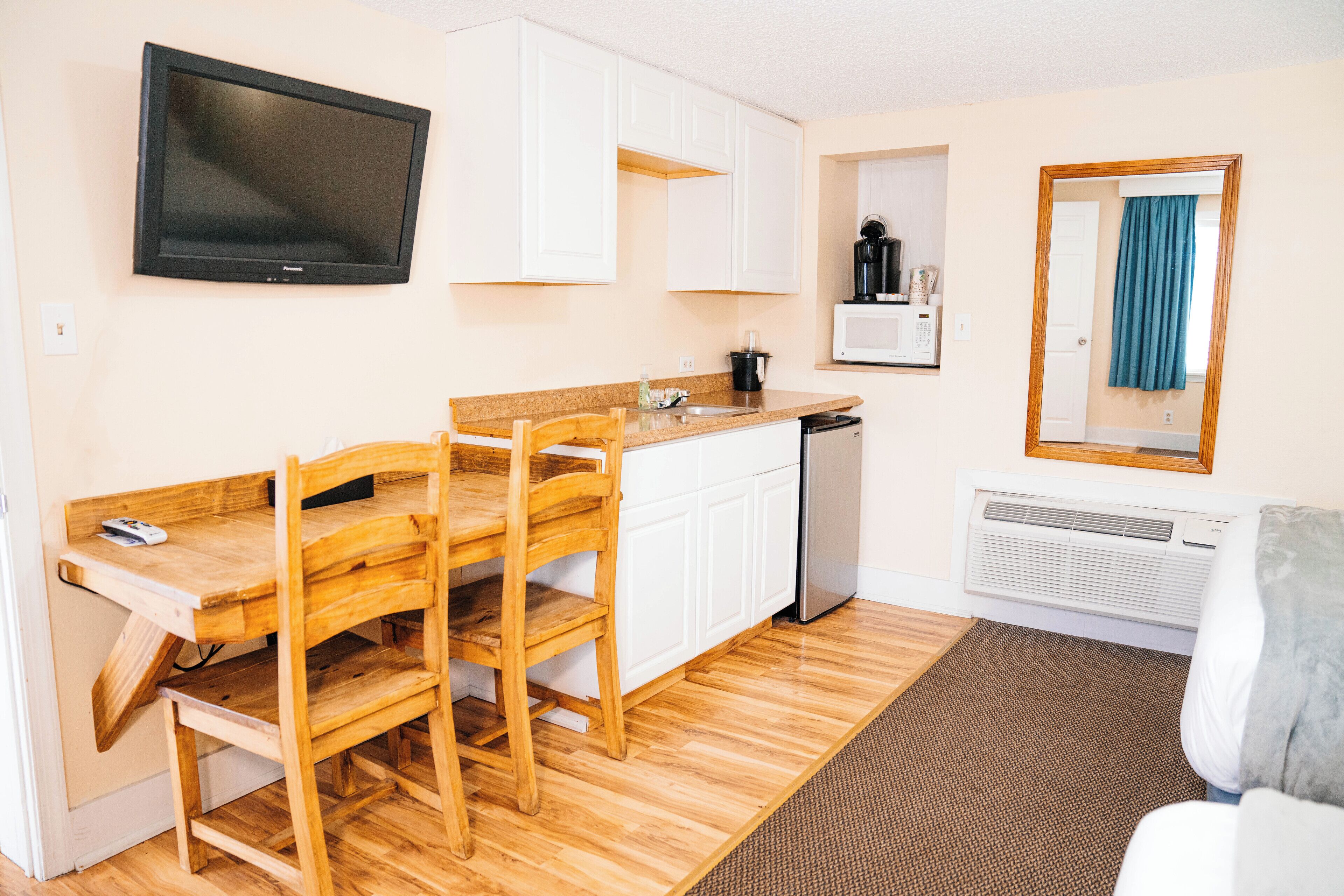 A compact kitchen with a wooden table and chairs, a built-in microwave, and a television mounted on the wall.