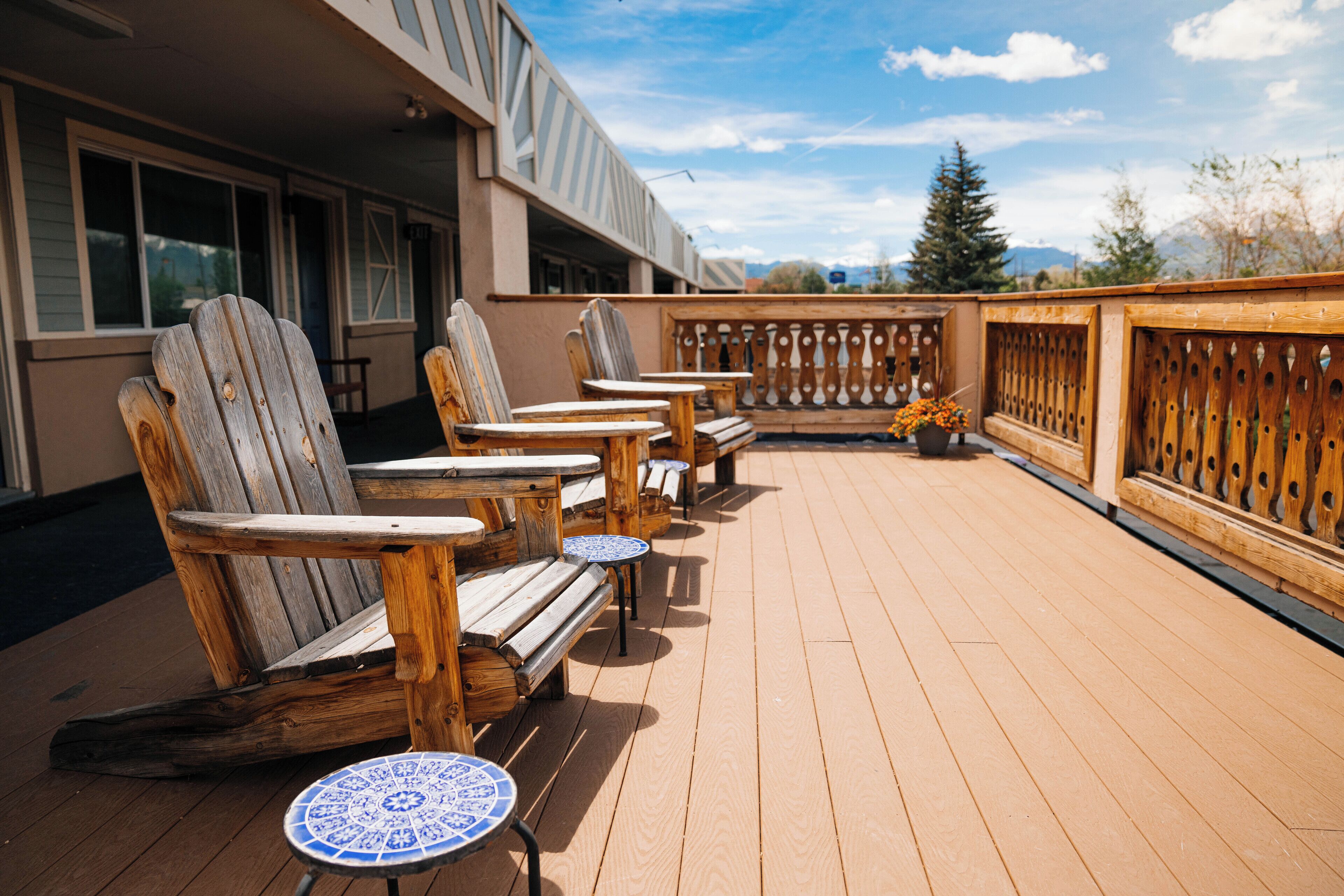 A wooden deck with Adirondack chairs and small round tables, overlooking a mountainous landscape.