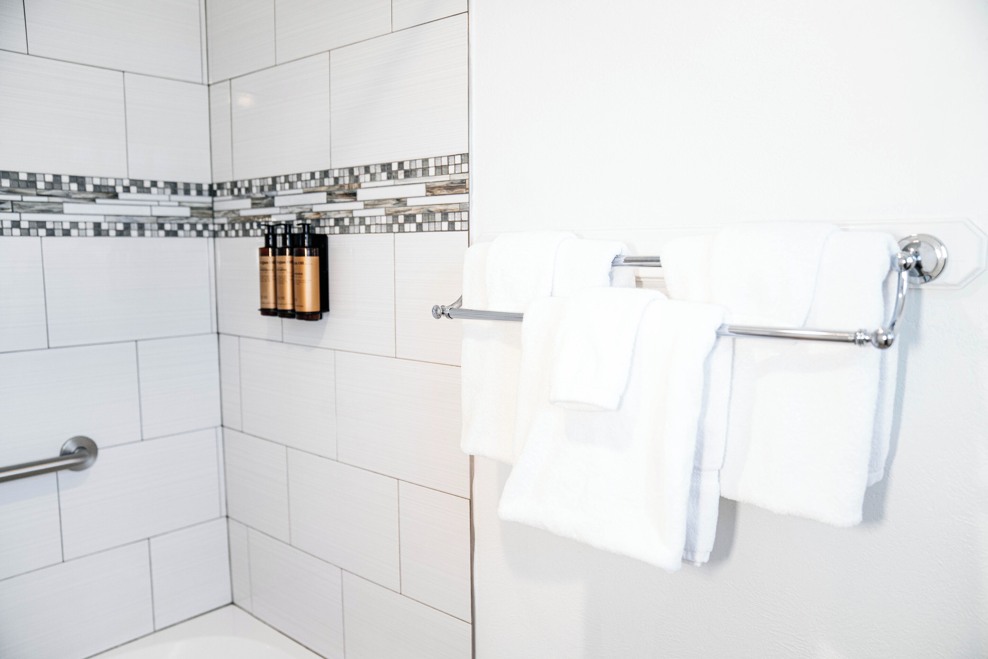 A bathroom with white tiles, a shower area, and a towel rack with two towels.