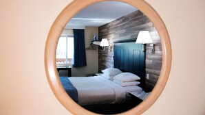 A hotel room with a bed, bedside lamps, a wooden accent wall, and a window with curtains. - Salida Inn & Monarch Suites (Salida)