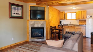 A cozy living room with a fireplace, a television mounted above it, and a sofa with a throw pillow. - Salida Inn & Monarch Suites (Salida)