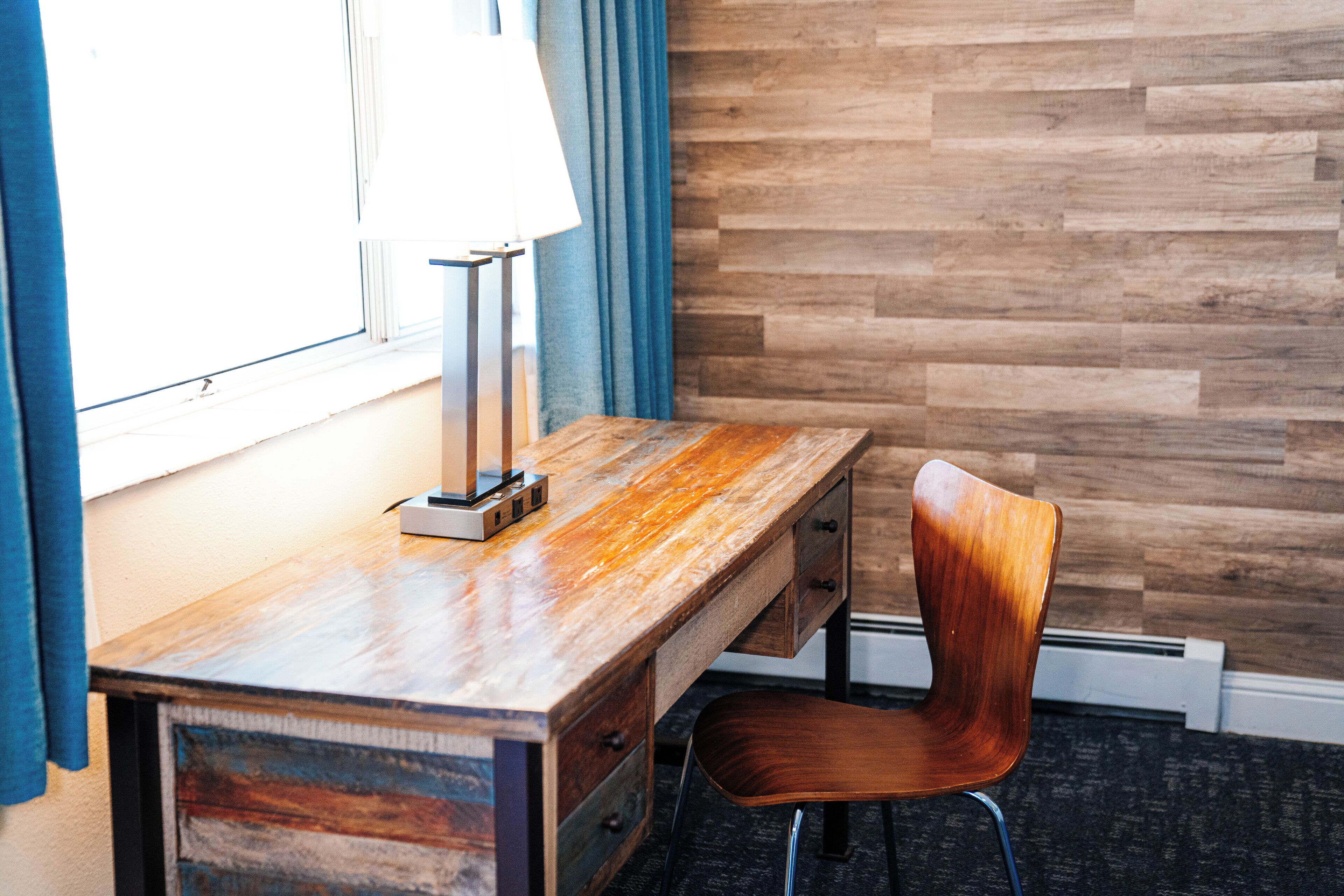 Un escritorio de madera con cajones y una silla, ubicado junto a una ventana con cortinas.