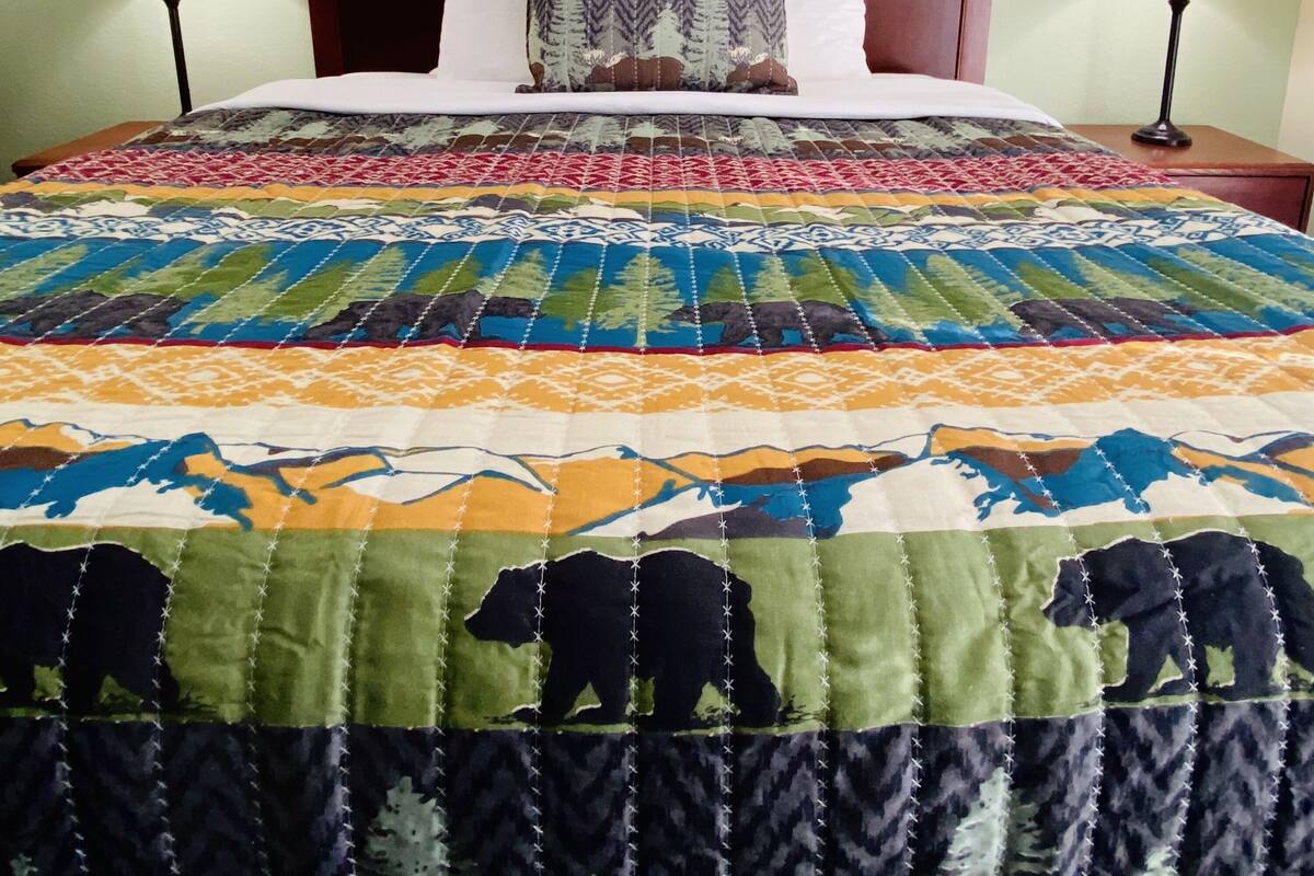 A bed with a colorful quilt, two bedside lamps, and a framed picture on the wall.