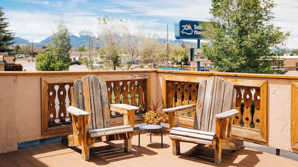 A wooden deck with Adirondack chairs and a small table, overlooking a mountainous landscape. - Salida Inn & Monarch Suites (Salida)