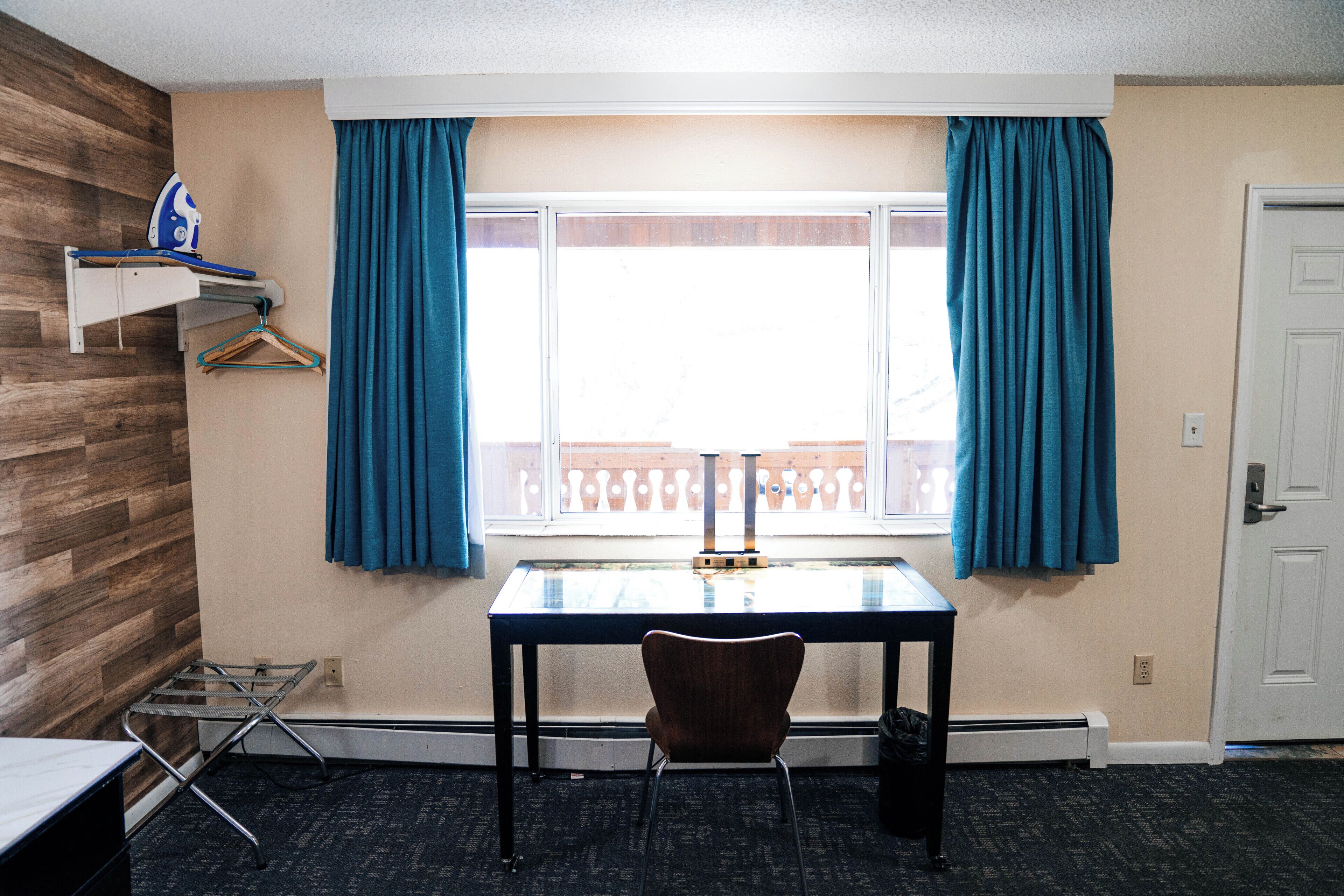 Una habitación con ventana, una mesa, una silla y un perchero.