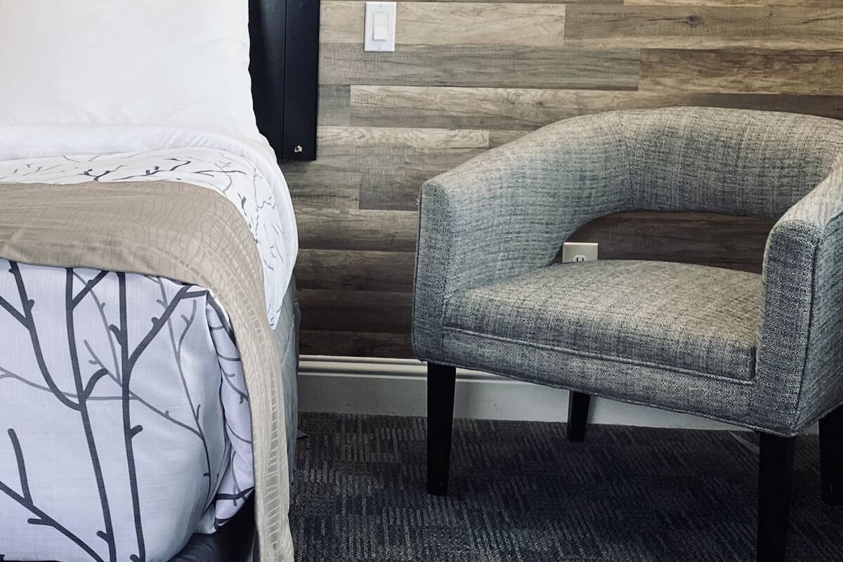 A hotel room with a bed, a chair, a wall-mounted lamp, and a wooden wall.