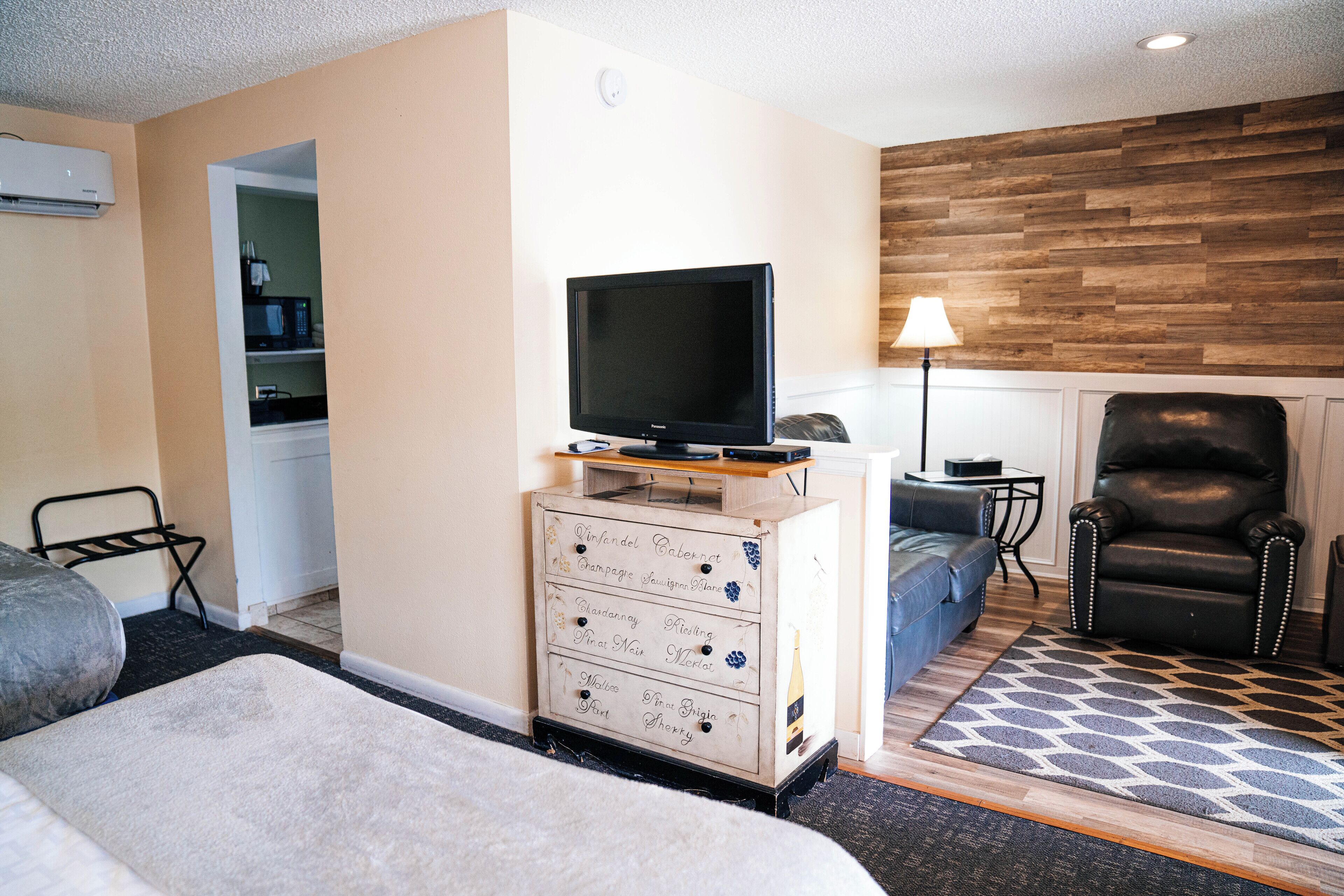A hotel room with a TV on a dresser, a sofa, a chair, and a patterned rug.