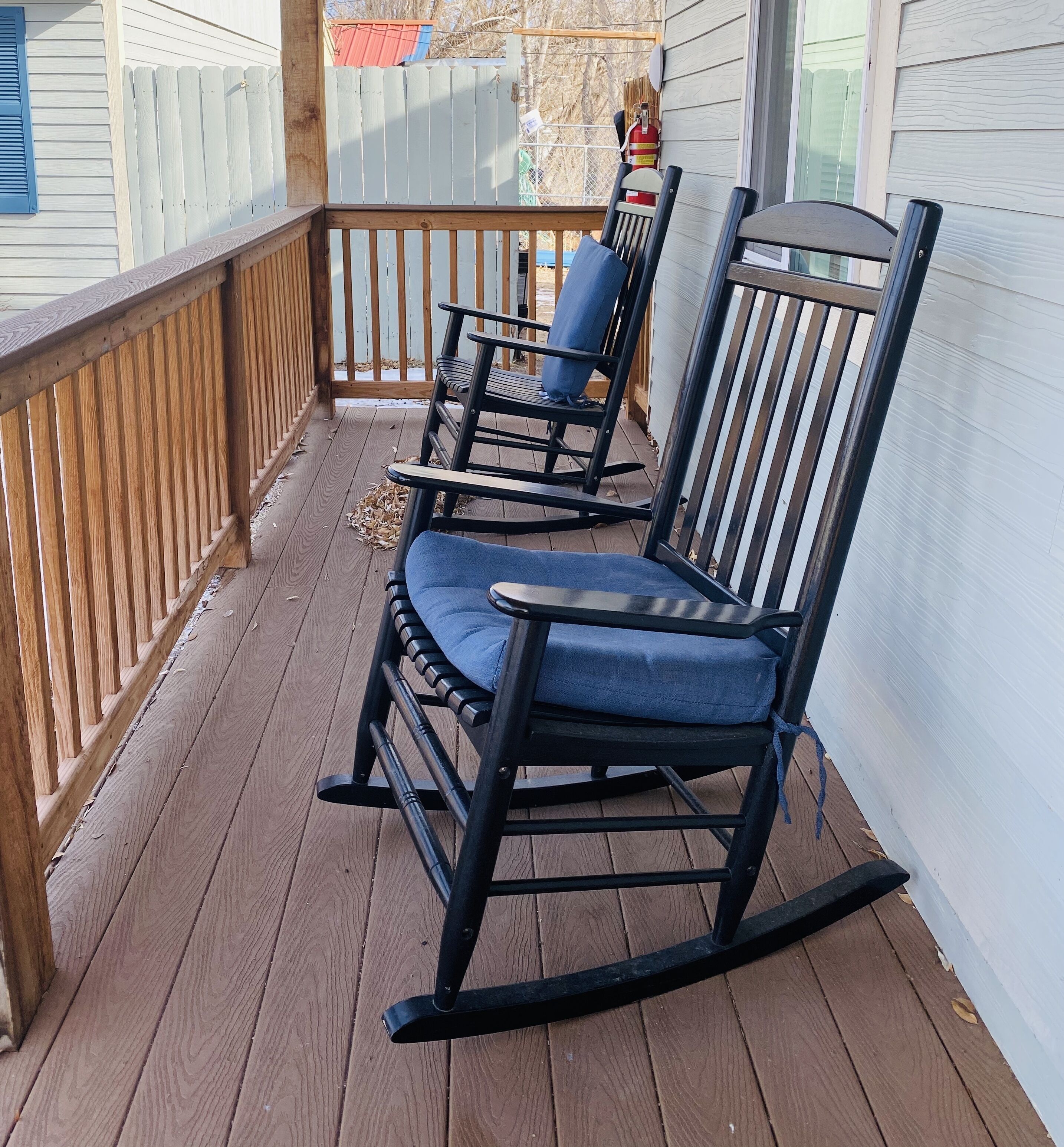 A wooden deck with three rocking chairs and a small table.