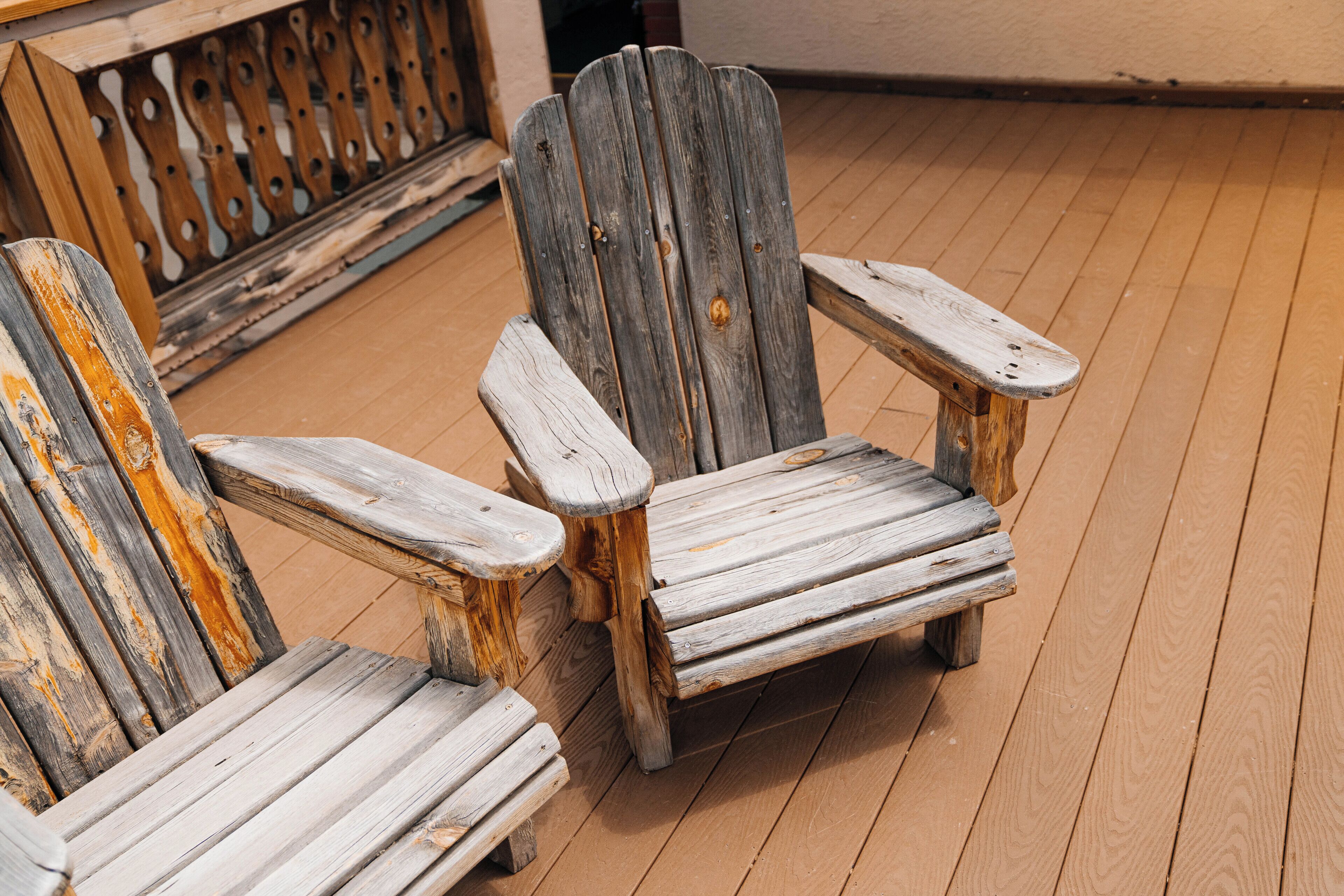 Two wooden Adirondack chairs with metal legs on a wooden deck.