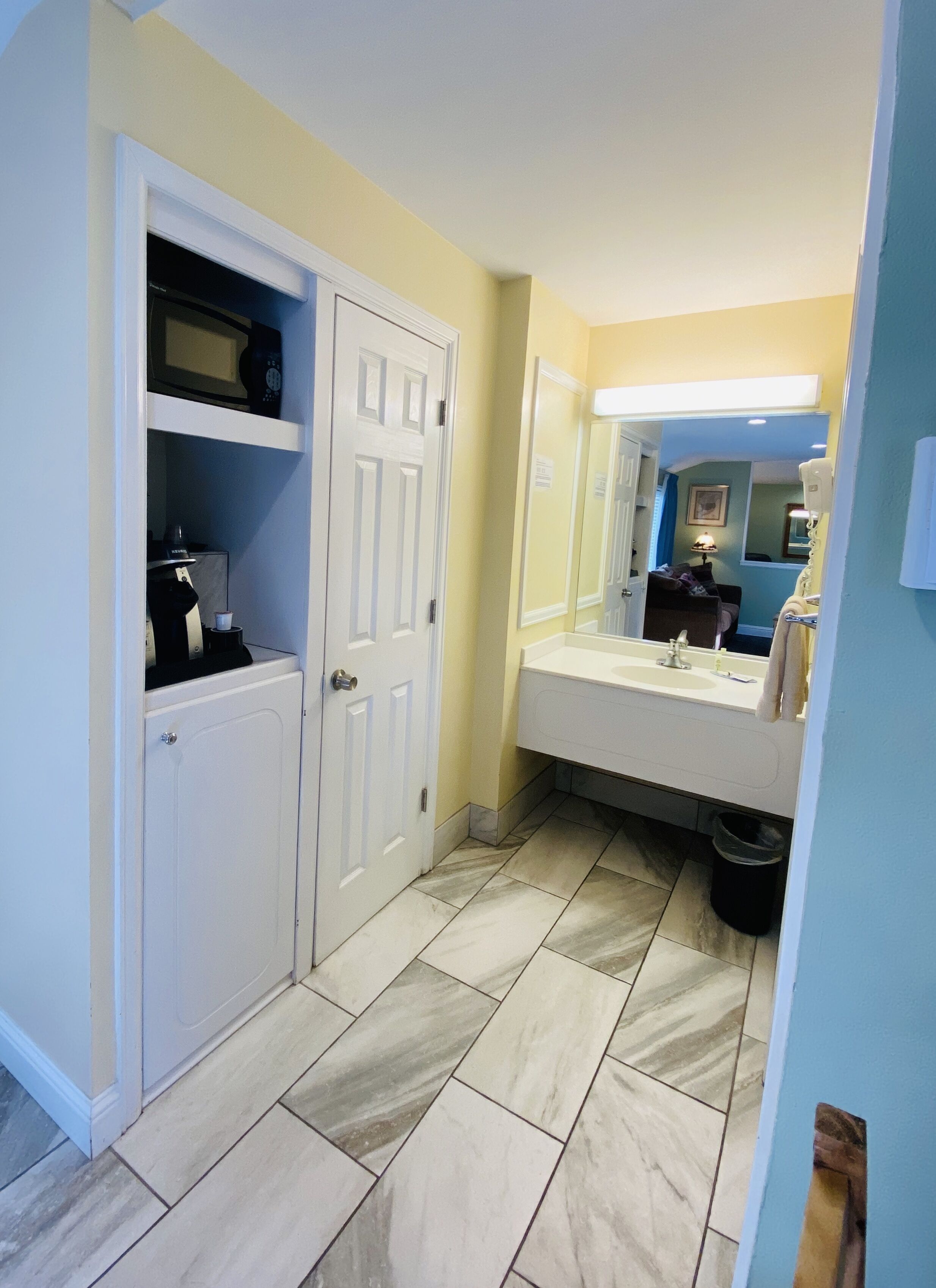 Un baño con tocador blanco, un espejo grande y piso de baldosas.
