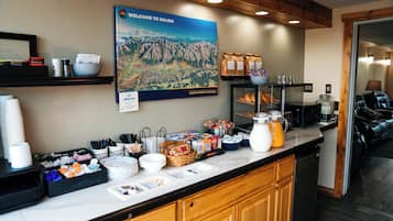 Un comptoir de petit-déjeuner avec des tasses à café, des bols et divers aliments. Un panneau d’accueil et une carte sont accrochés au mur.