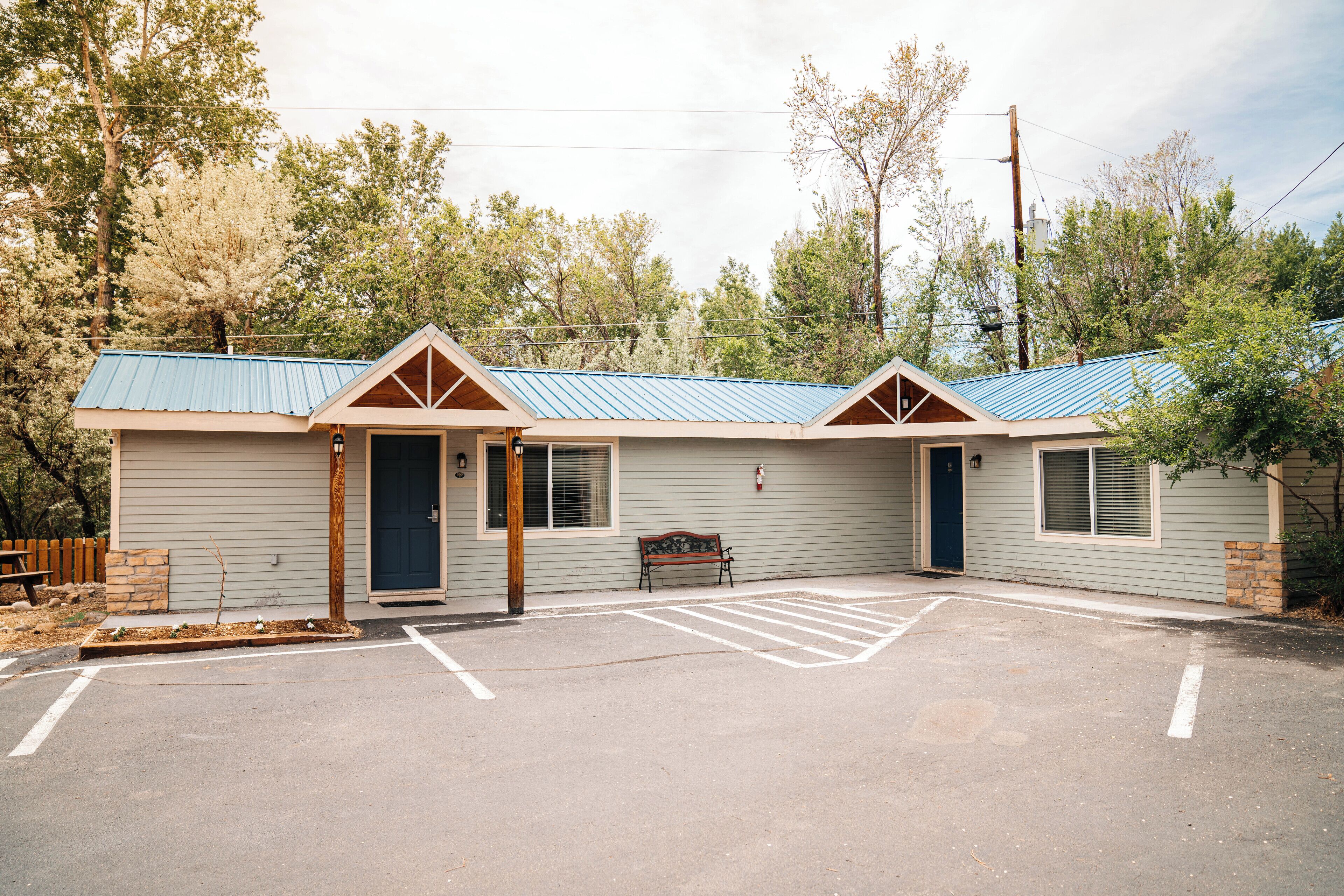 A motel with a blue roof, a bench outside, and a parking lot.