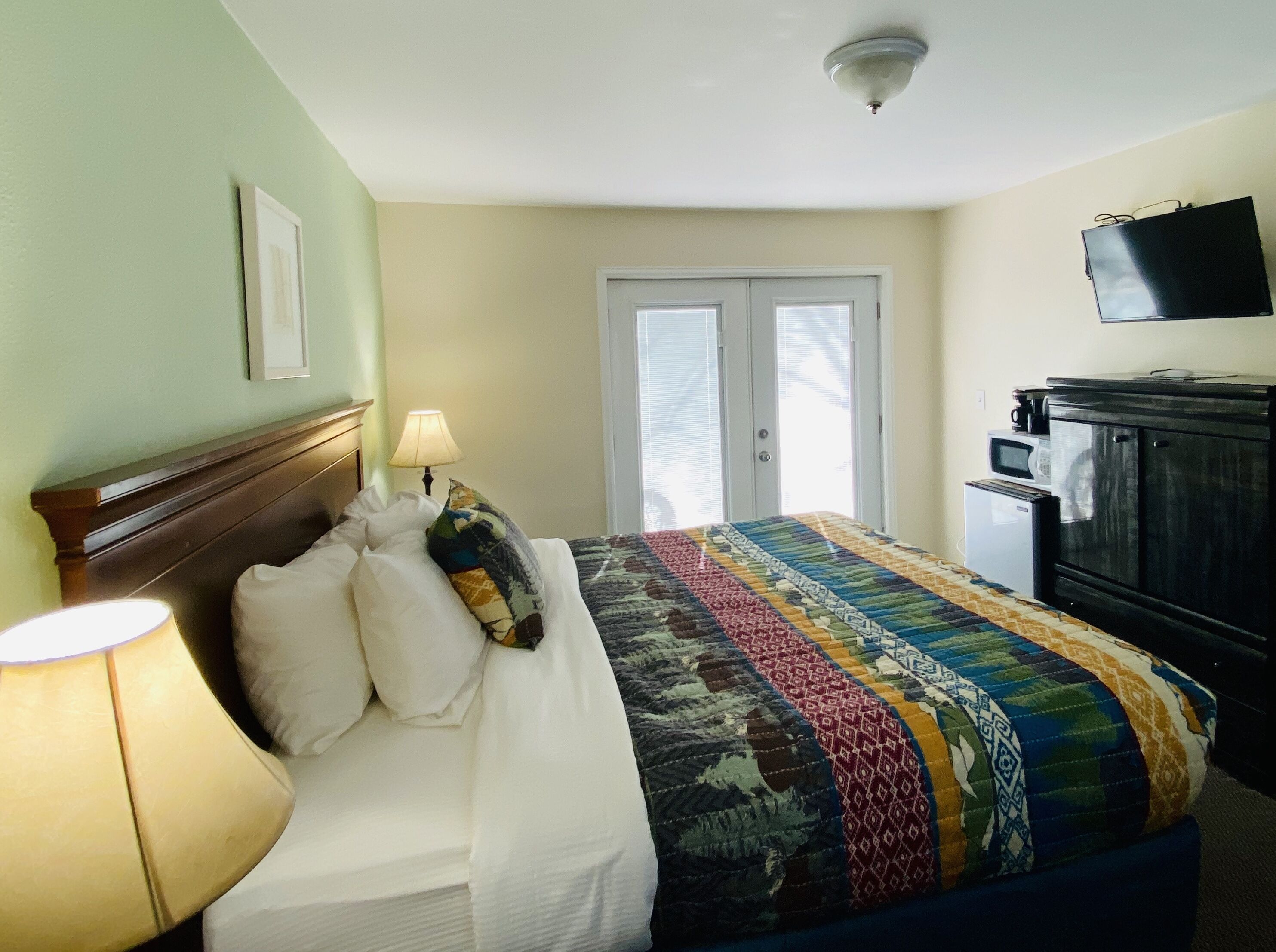 A hotel room with a bed, a lamp, a television, and a microwave.