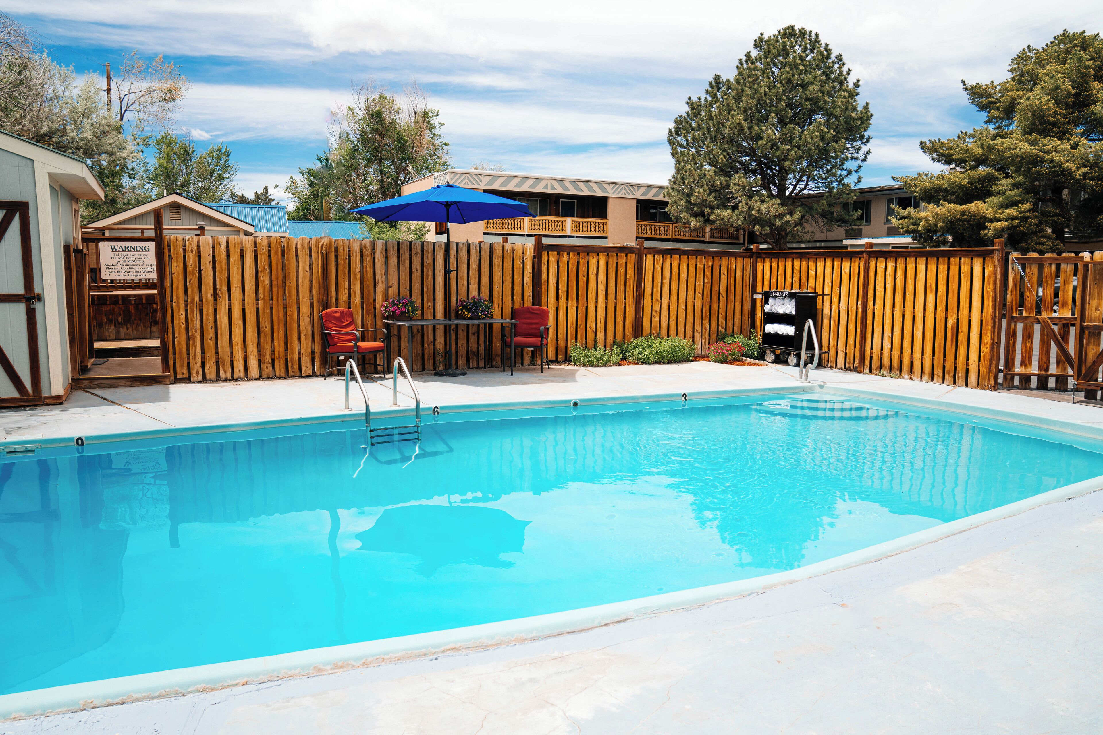 A swimming pool with a wooden fence, a covered patio area, and a building in the background.