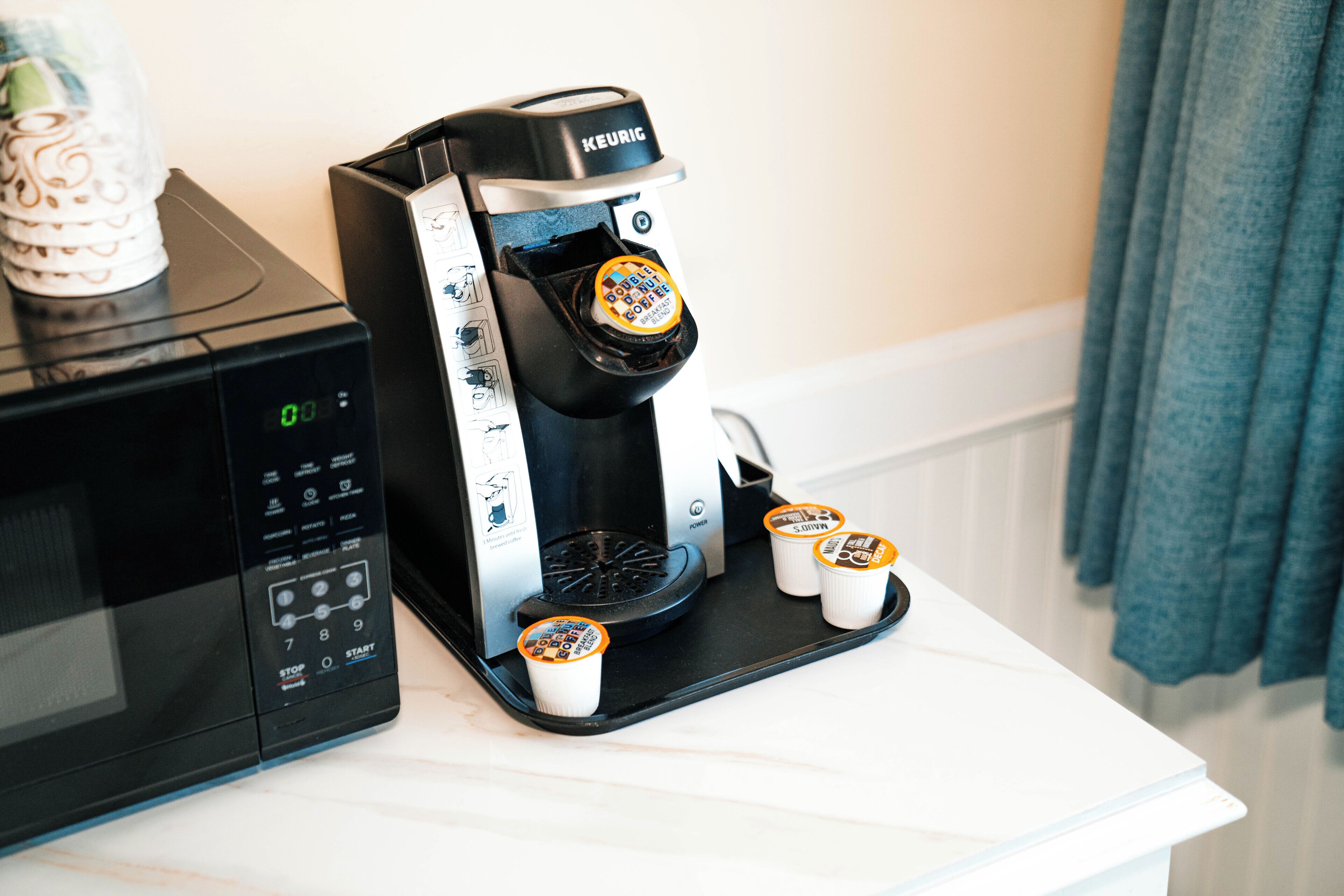 Una cafetera Keurig con tres cápsulas de café sobre una encimera blanca, junto a un microondas.