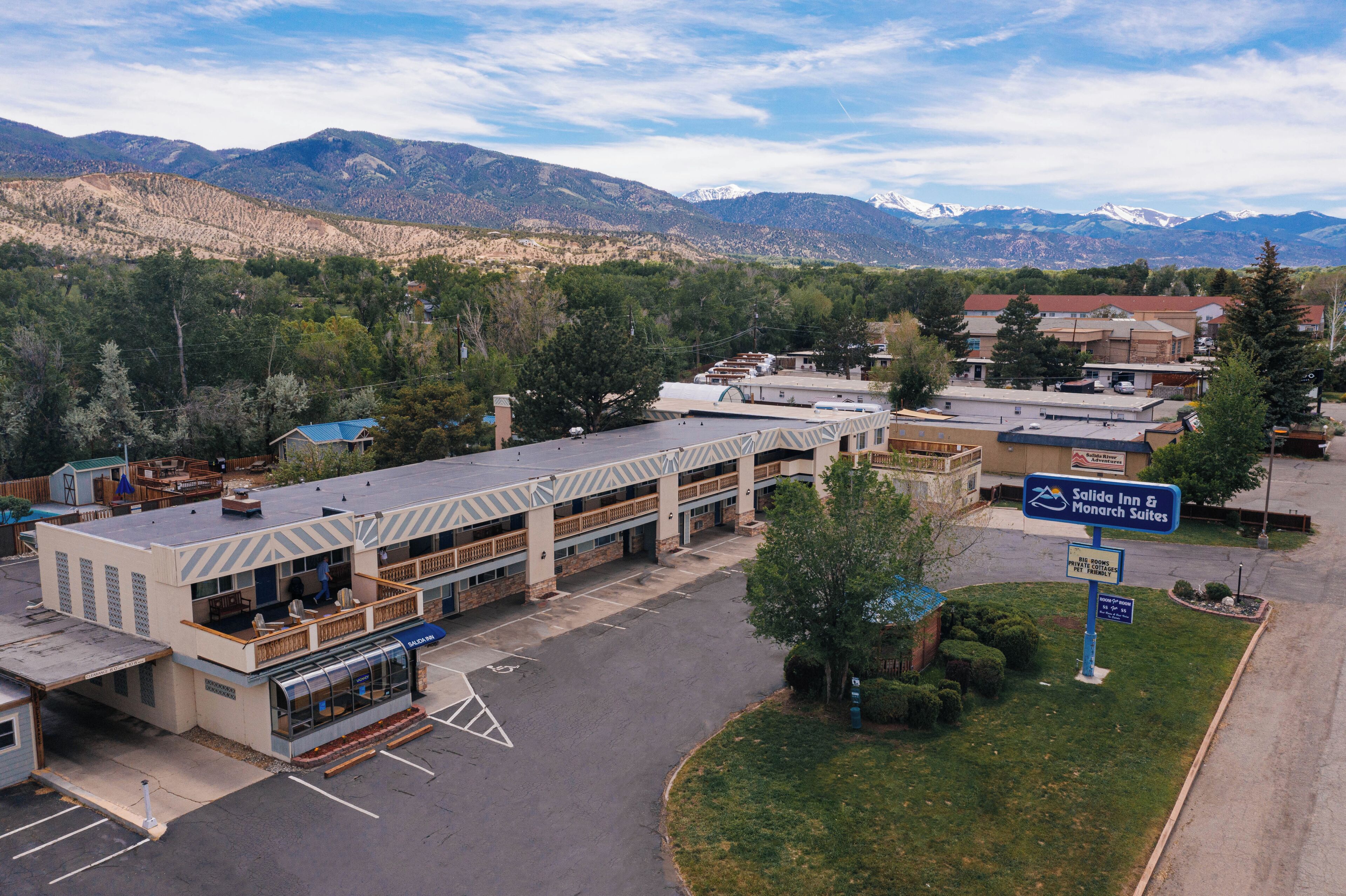 A hotel with a parking lot, a sign for Salida Inn & Monarch Suites, and mountains in the background.
