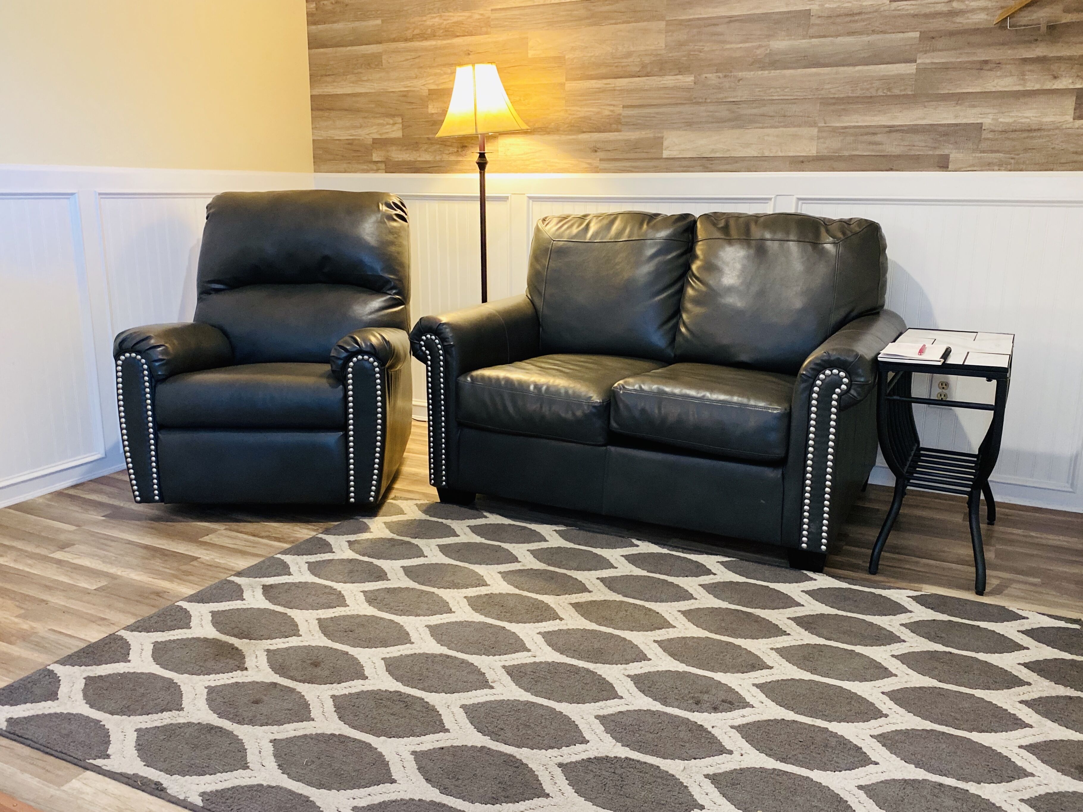 A room with two black leather armchairs with white studs, a small black side table with a lamp, and a patterned rug.