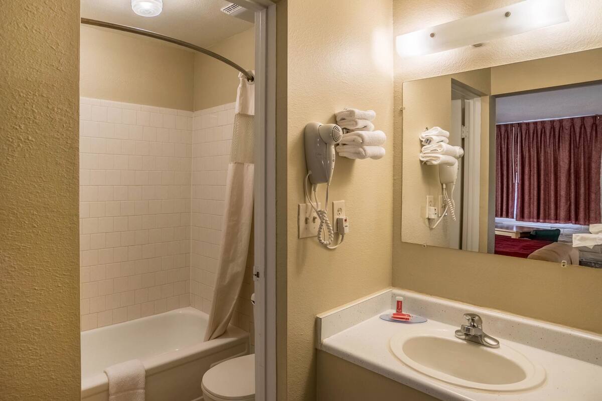 Ein Badezimmer mit Badewanne, Toilette und Waschbecken mit Spiegel. Handtücher und ein Haartrockner befinden sich an der Wand.