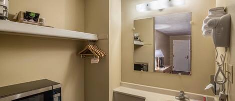 A hotel bathroom with a microwave, a sink, a hairdryer, and a mirror.