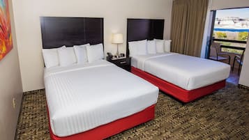 A hotel room with two beds, a nightstand, a lamp, and a view of the outdoors.