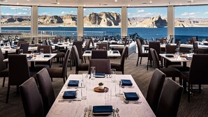 A restaurant with tables set for dining, large windows offering a view of the sea and cliffs.