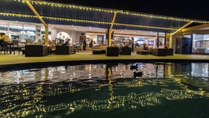An outdoor pool area with seating and a bar, surrounded by a covered walkway with string lights.