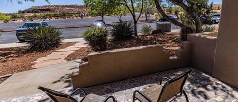 A patio with two chairs, a tiled floor, and a view of a parking lot with cars and a hilly landscape.