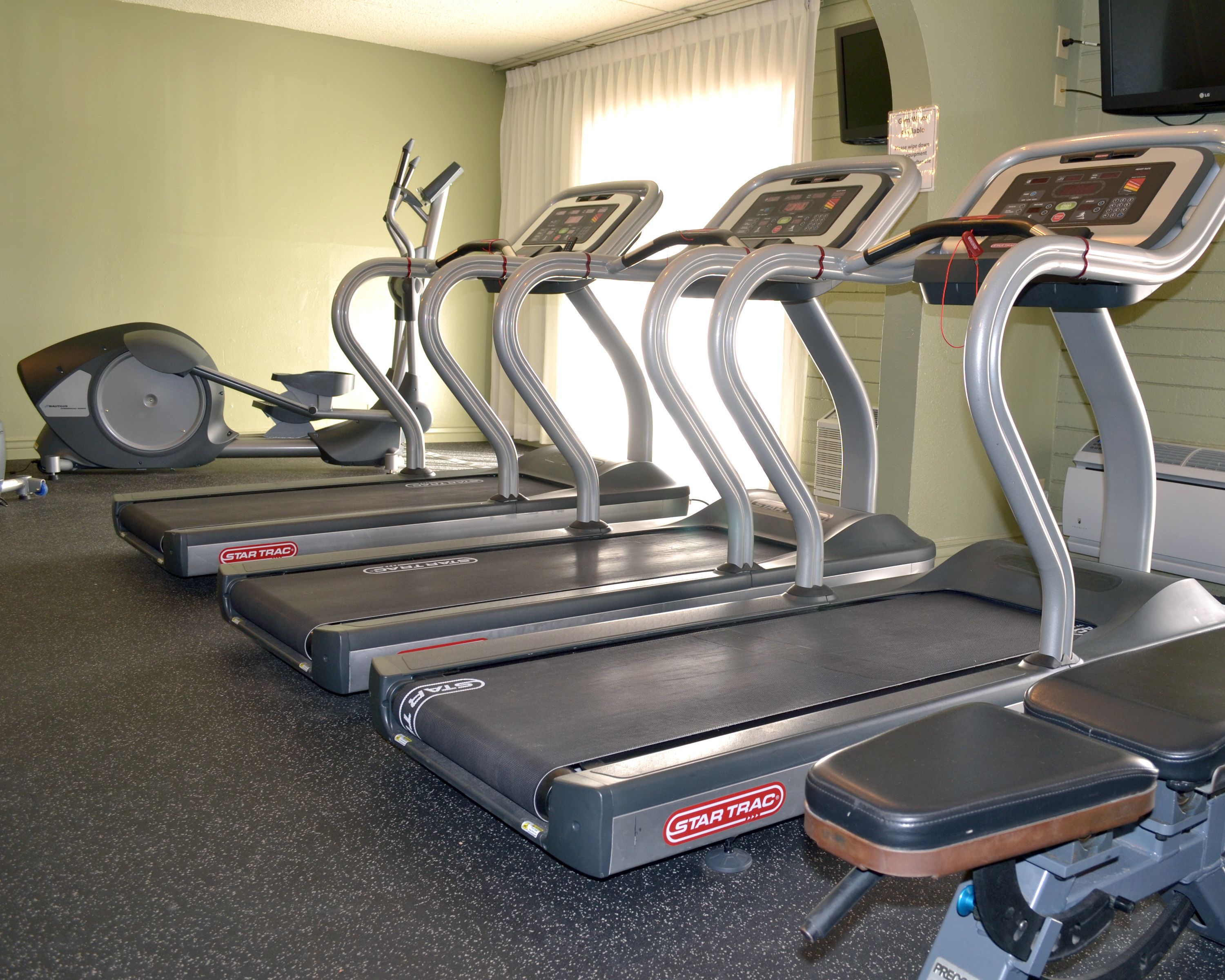 Cuatro cintas de correr StarTrac en un gimnasio con un muro espejado y una ventana con cortinas.