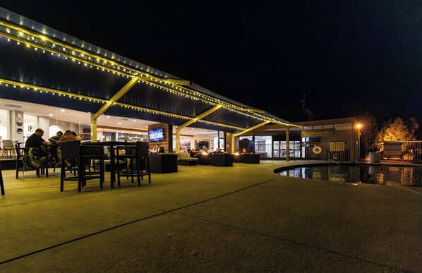 An outdoor seating area with tables and chairs, a pool, and a building with a covered patio.