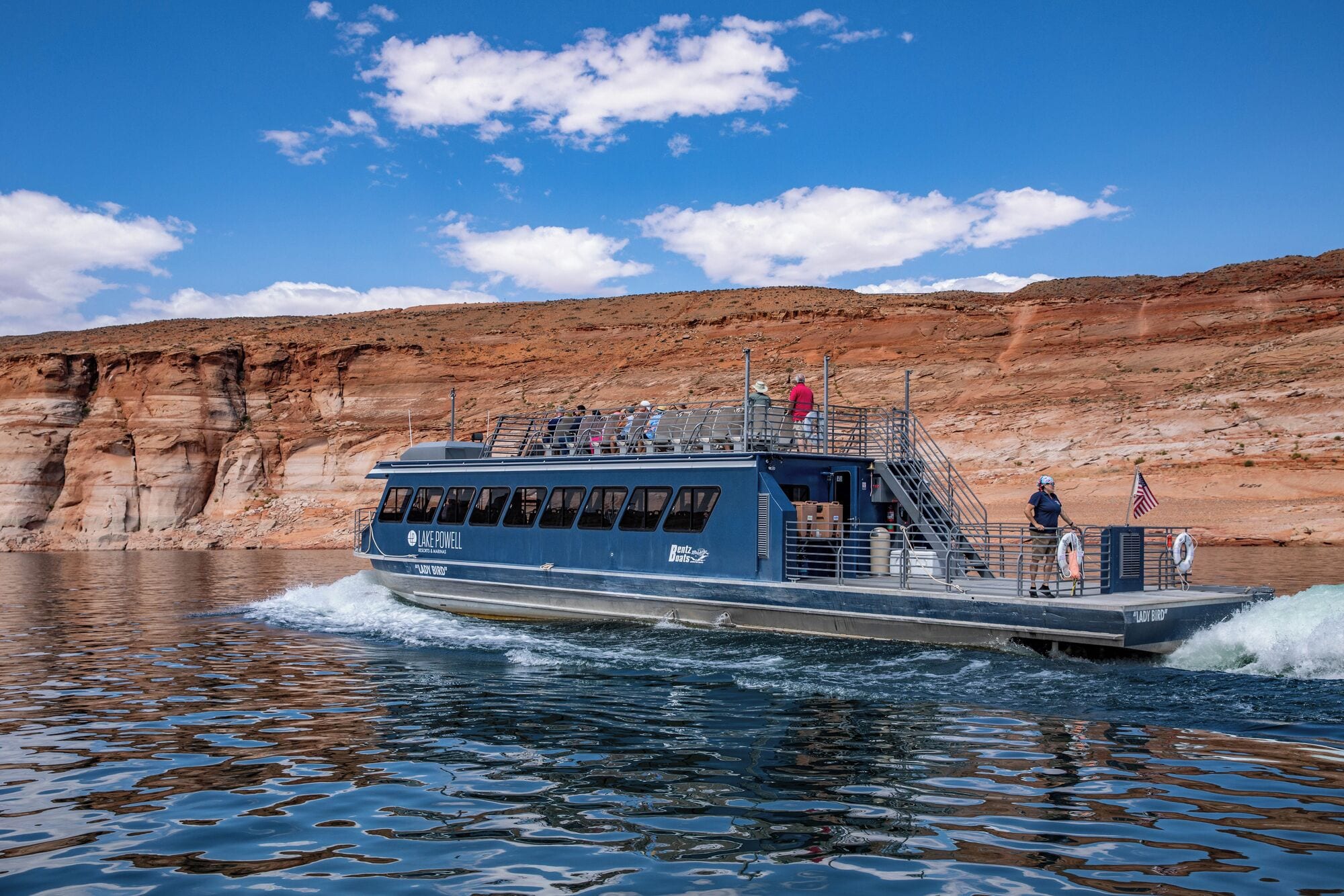 A boat named 'Lady Bird' with a blue exterior, passengers on deck, and a rocky landscape in the background.