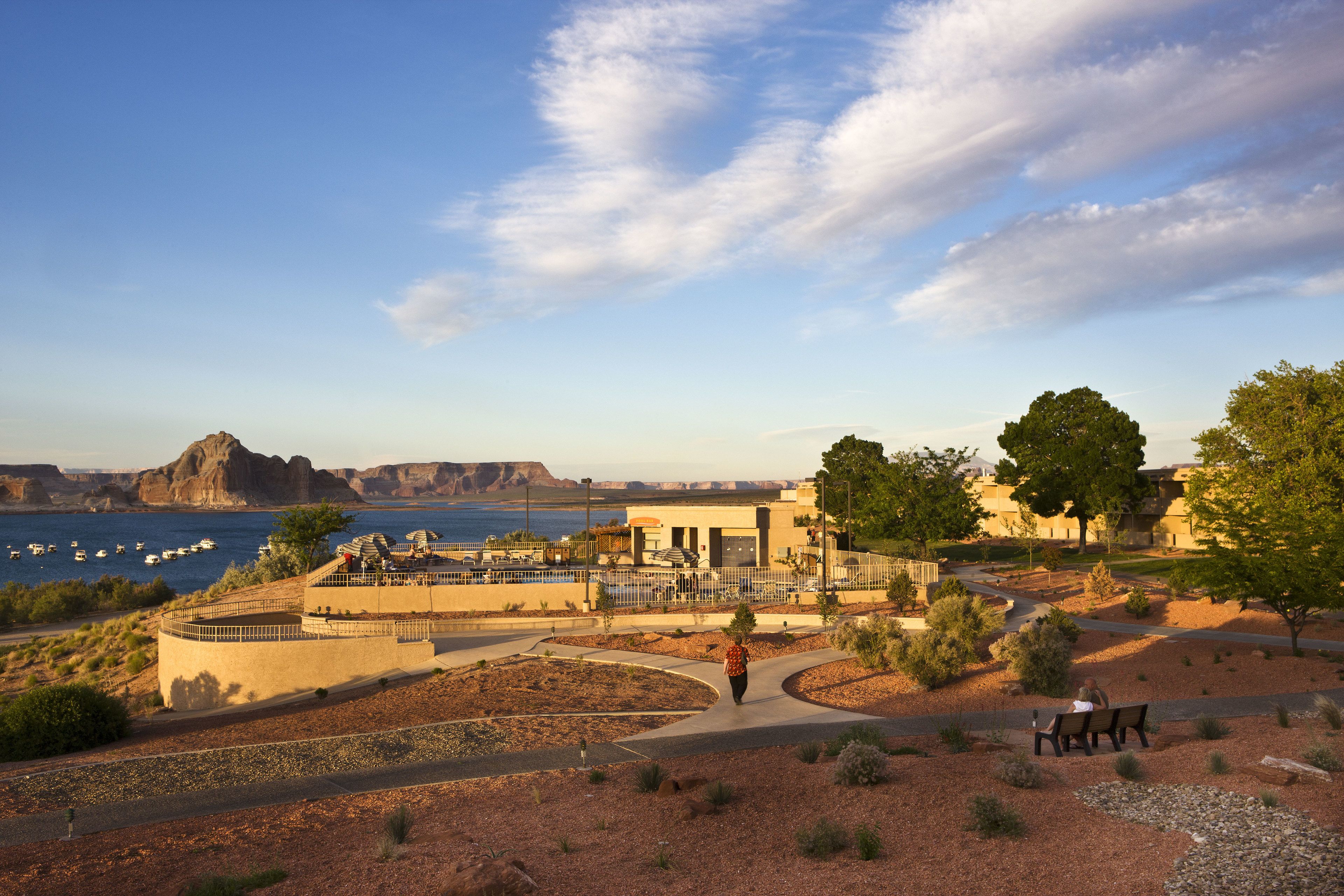 A park with a walking path, benches, and a view of the water and distant mountains.