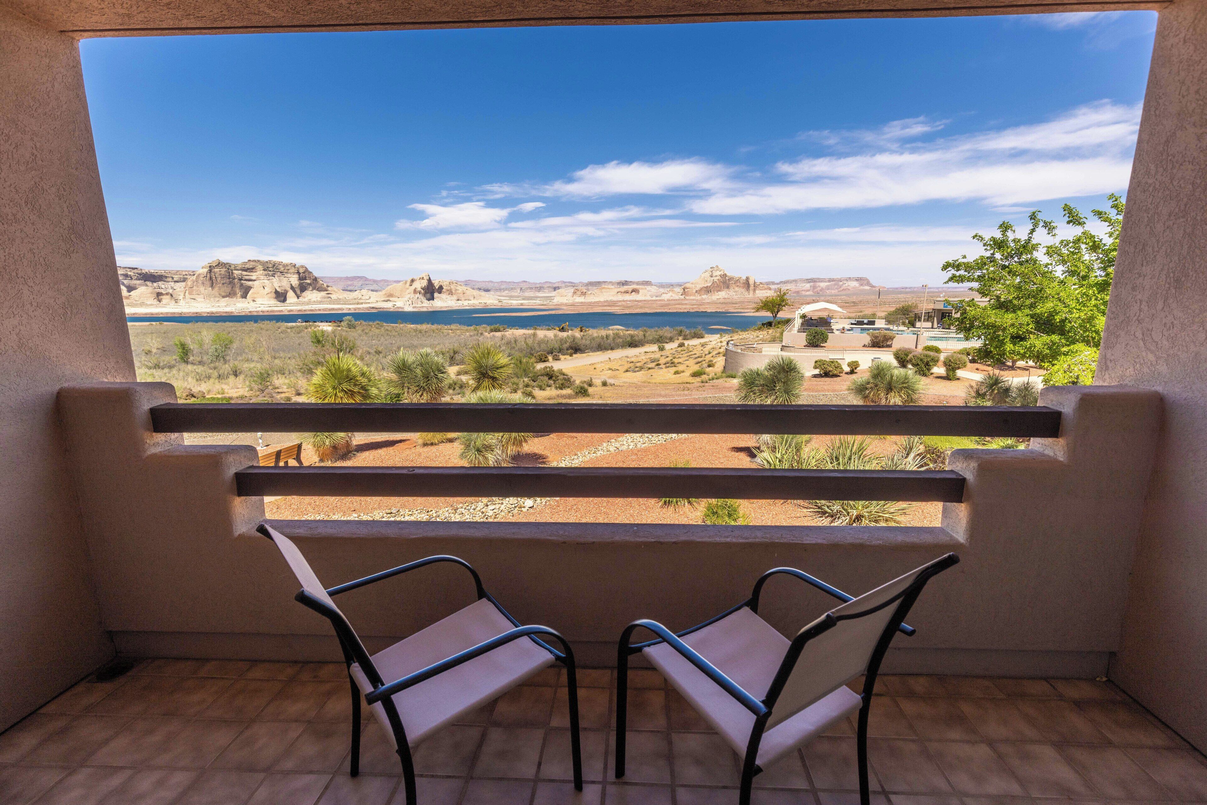 En balkon med to stole, en pool og udsigt over et ørkenlandskab.