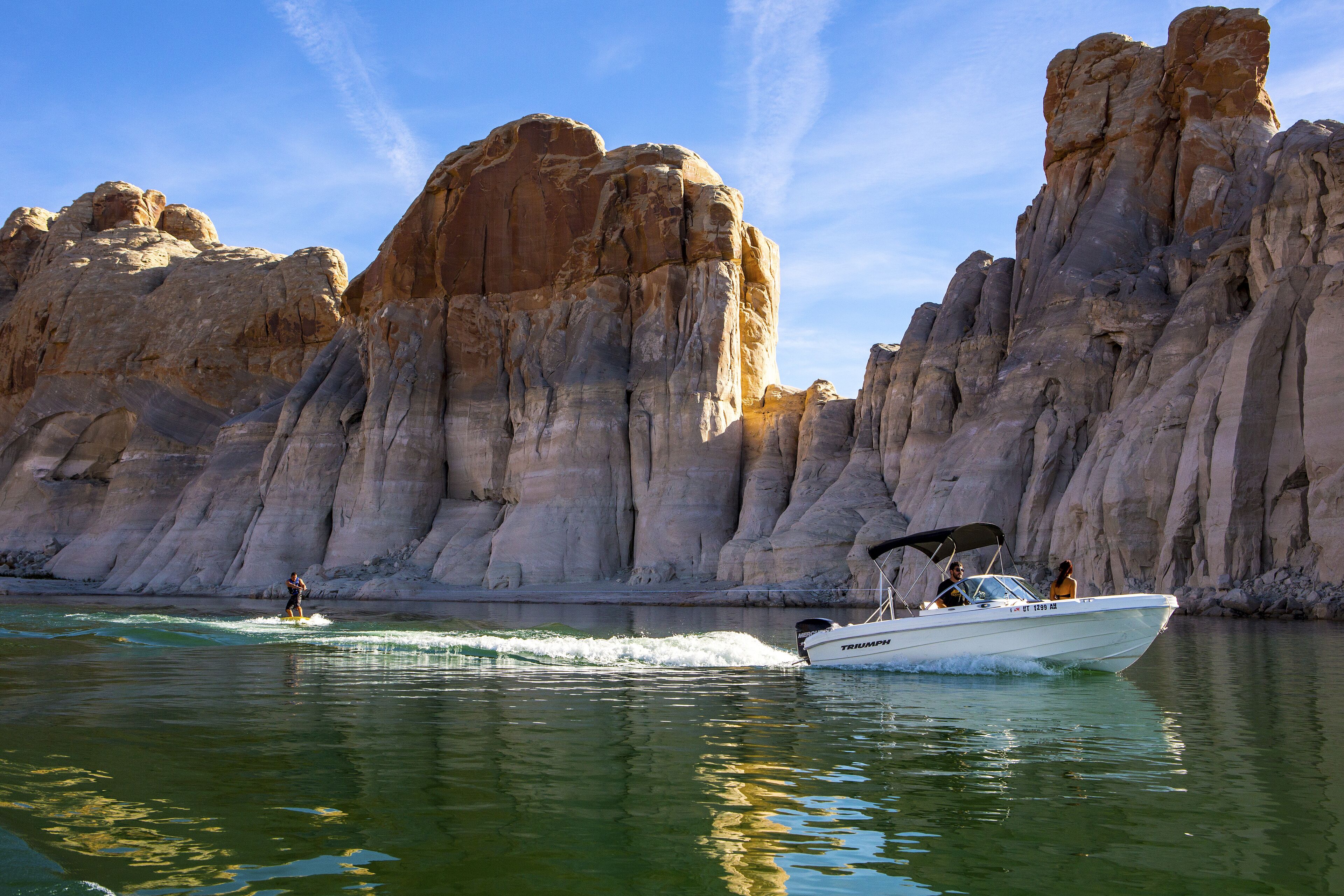 A boat on a calm river with rocky cliffs in the background.