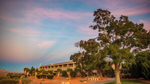 A building with a flat roof and multiple windows, surrounded by landscaped gardens with various shrubs and a large tree.