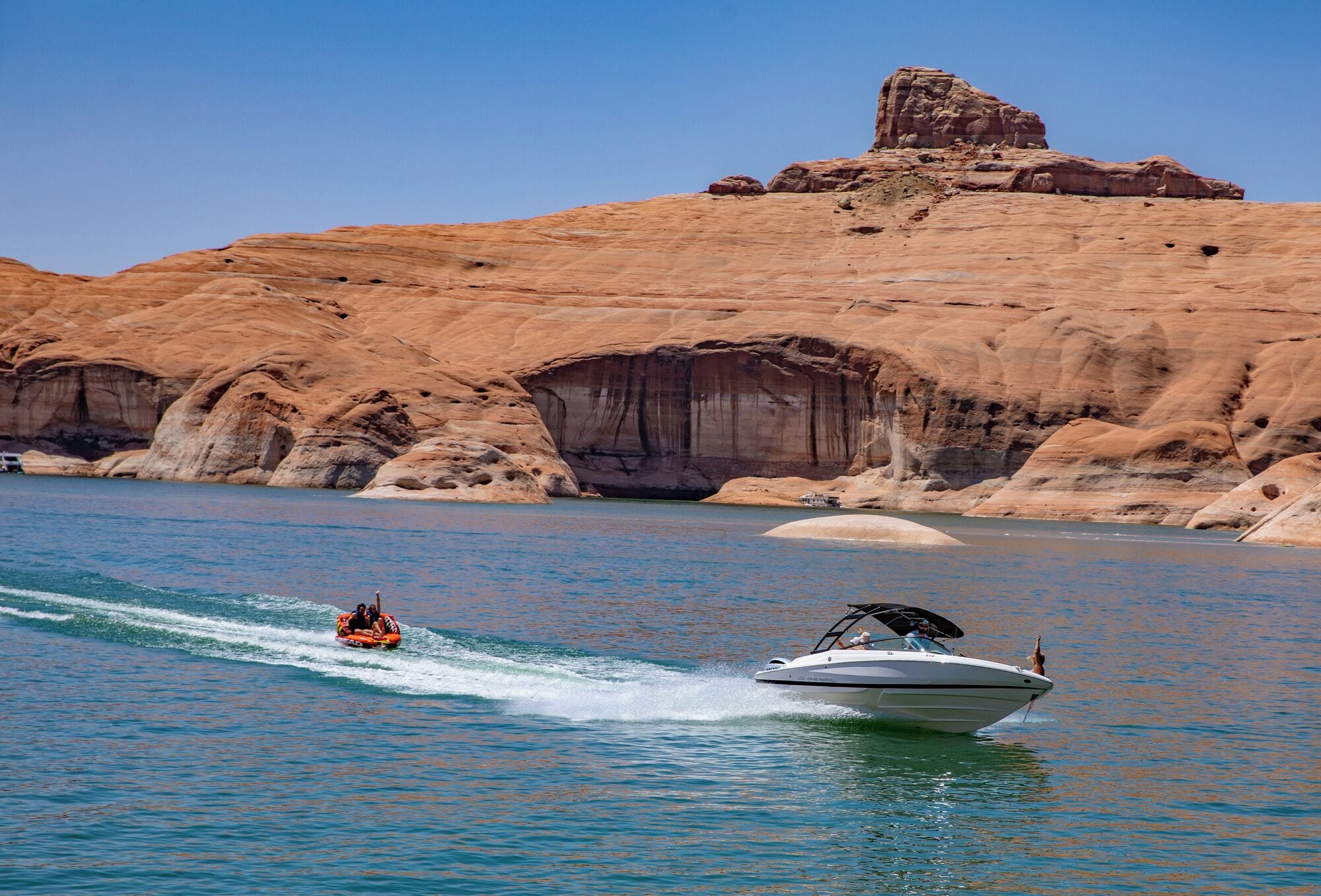 A boat on a calm lake with a rocky cliff in the background.