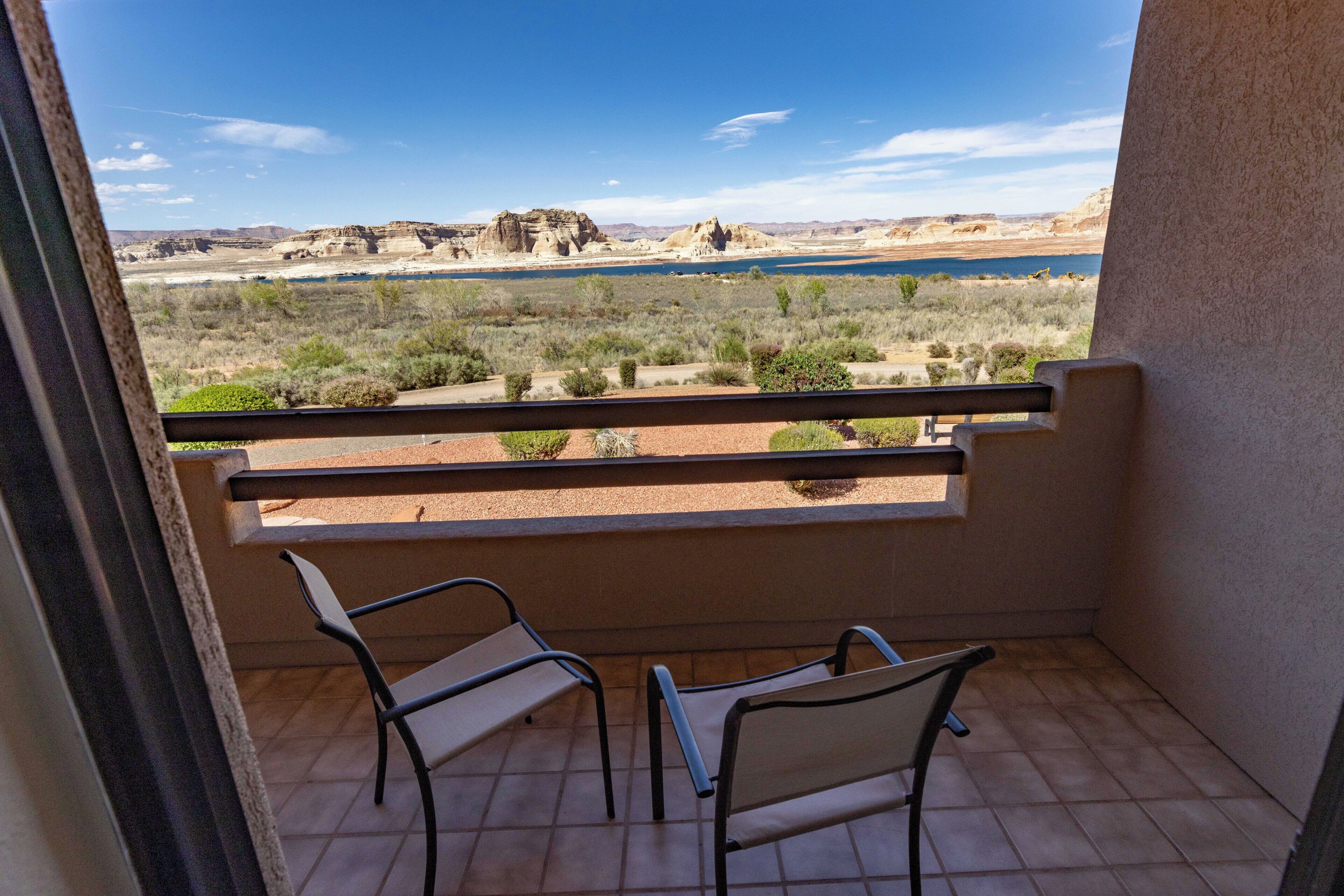 A balcony with two chairs, a view of a desert landscape with rock formations and a body of water.