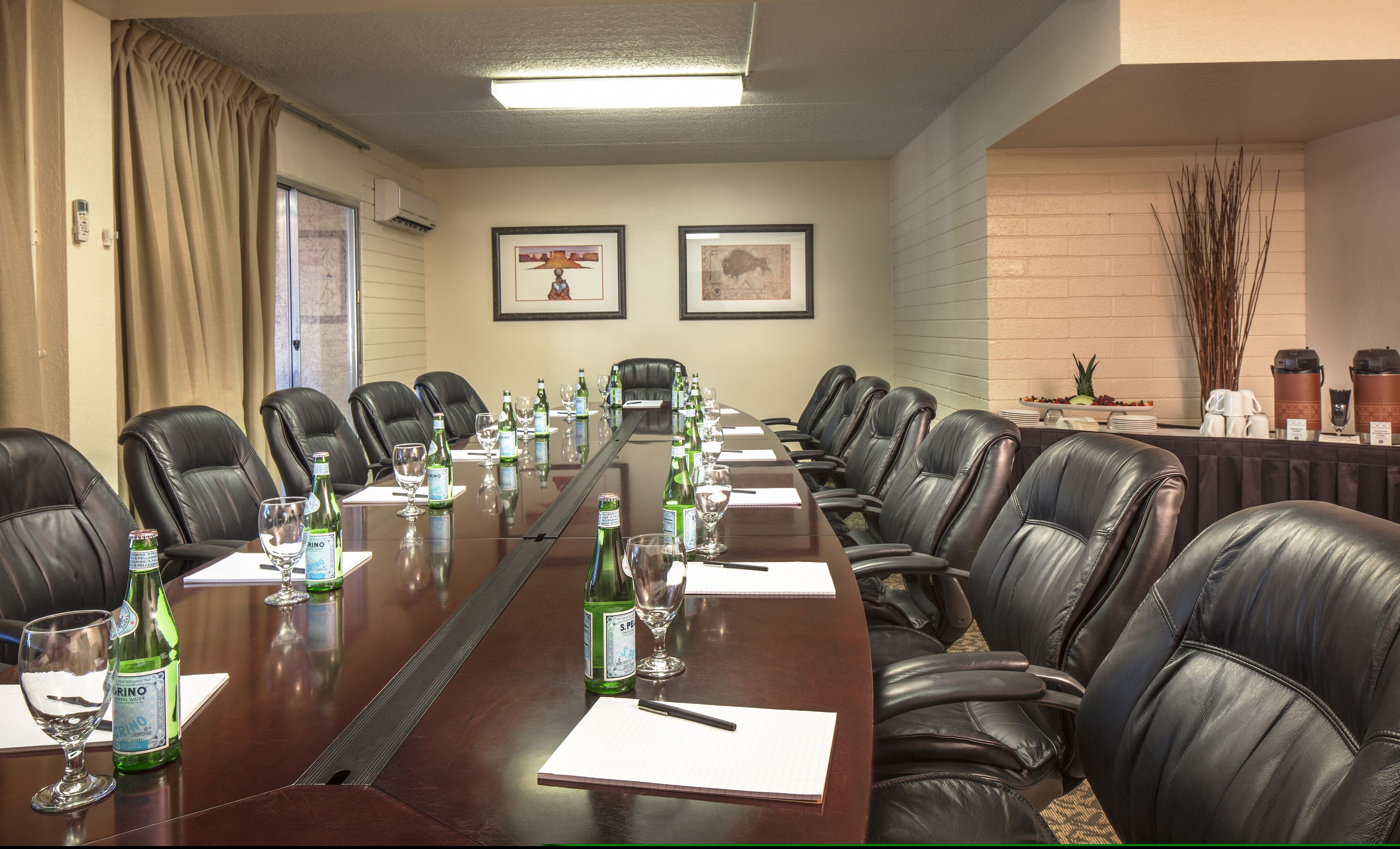 A conference room with a long table, leather chairs, and a buffet area with food and drinks.