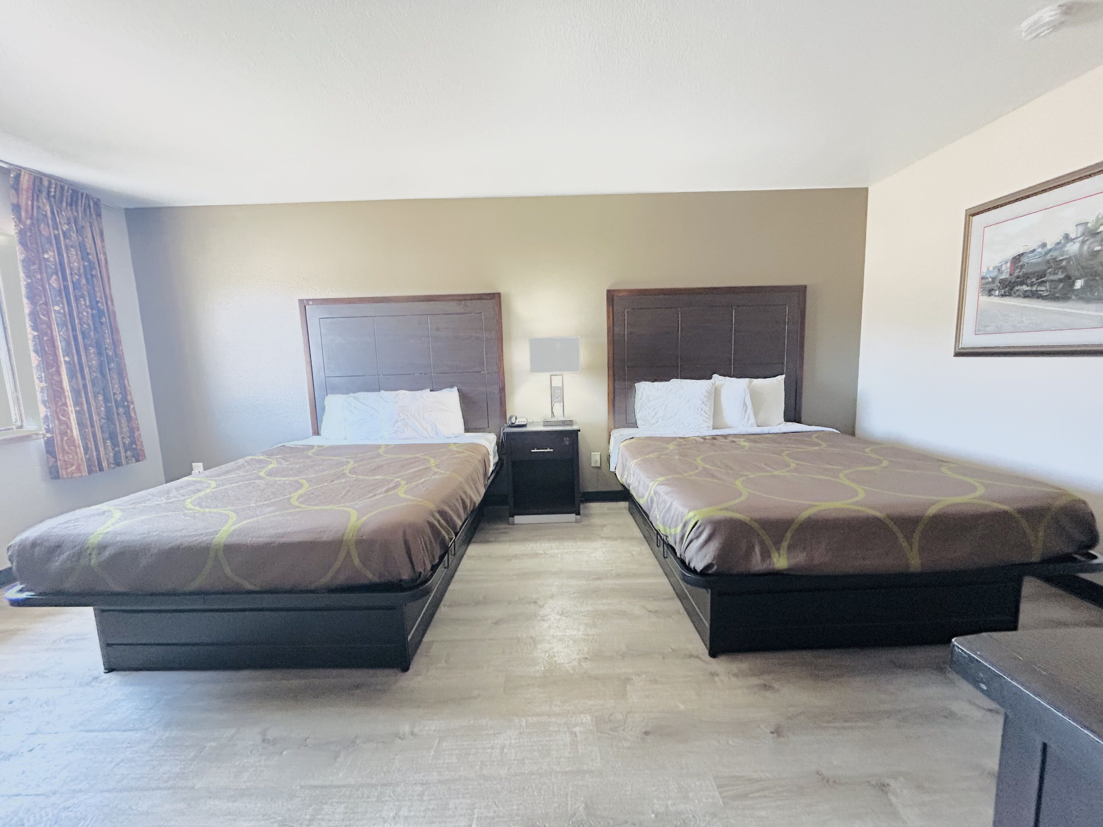 A hotel room with two beds, a nightstand, a lamp, and a framed picture on the wall.
