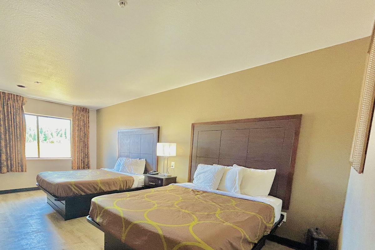 A hotel room with two beds, a nightstand with a lamp, and a window with curtains.