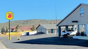 A Super 8 motel with a parking lot, a white car parked inside, and a mountainous backdrop. - Super 8 by Wyndham Williams West Route 66/Grand Canyon Area (Williams)
