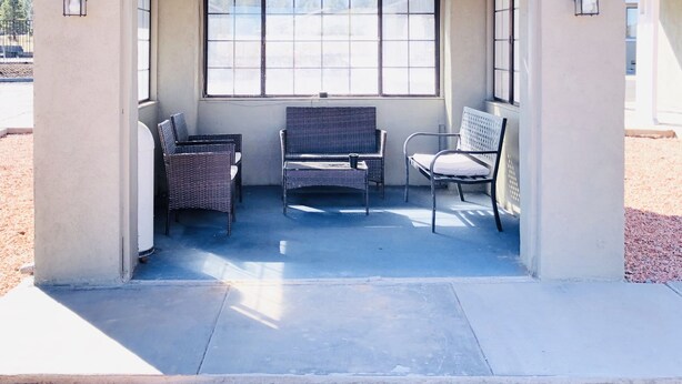 A covered outdoor seating area with two wicker chairs and a table, a large window, and a small roof structure. - Super 8 by Wyndham Williams West Route 66/Grand Canyon Area (Williams)