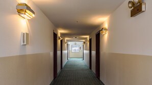 A hotel hallway with patterned carpet, wall-mounted lights, and doors on either side. - Super 8 by Wyndham Williams West Route 66/Grand Canyon Area (Williams)