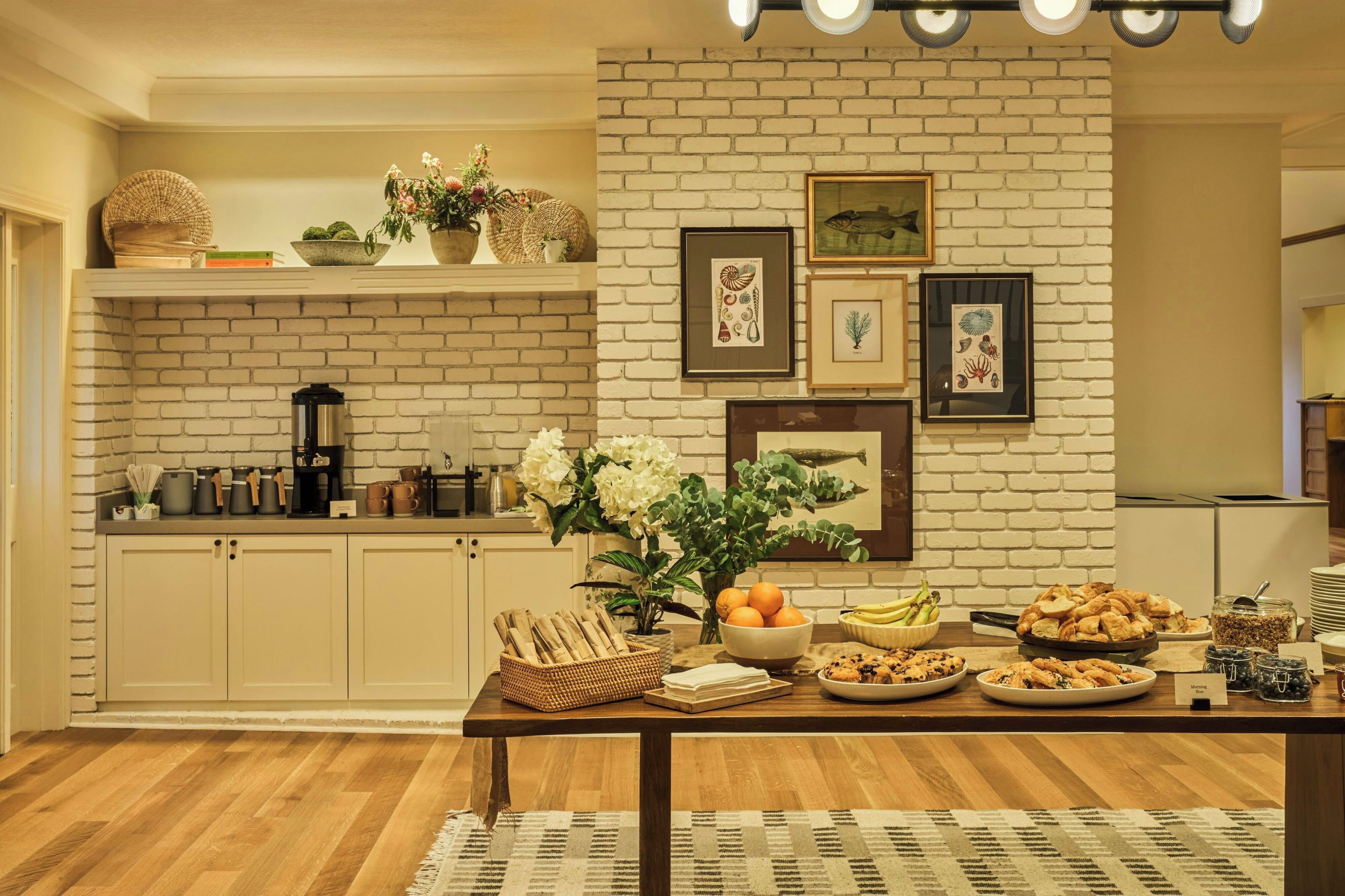 A breakfast setup with a table, coffee maker, and various food items.