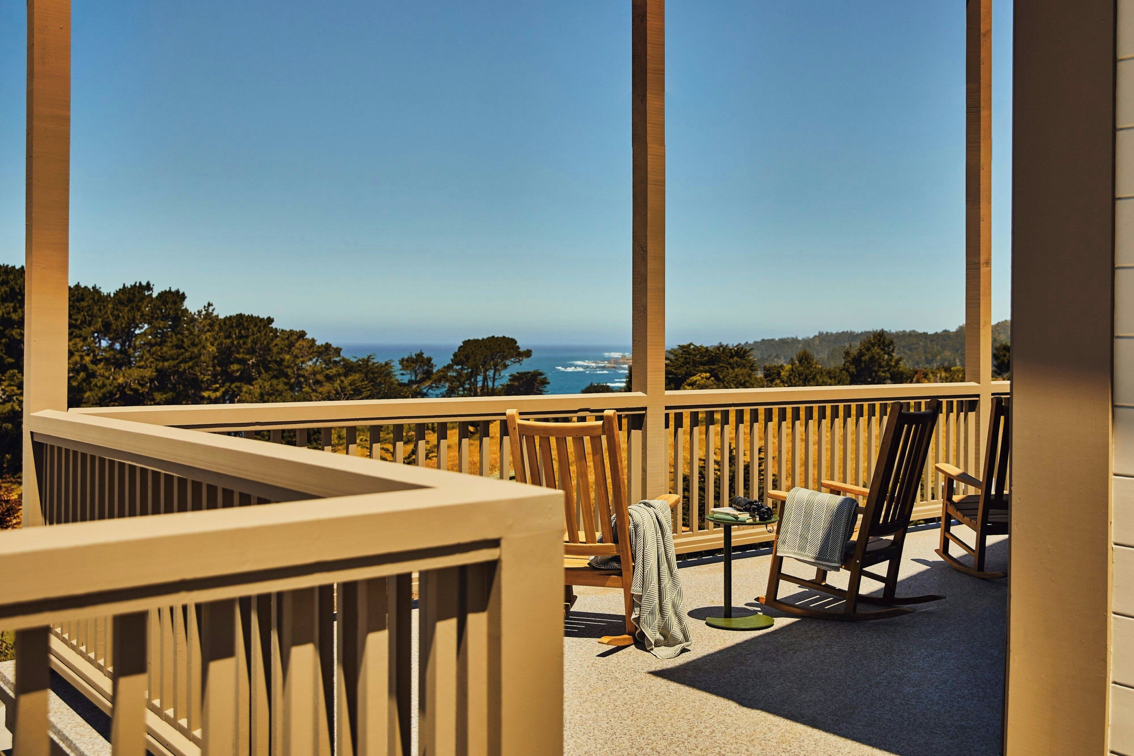 A balcony with a view of the ocean, a chair, a small table, and a book.