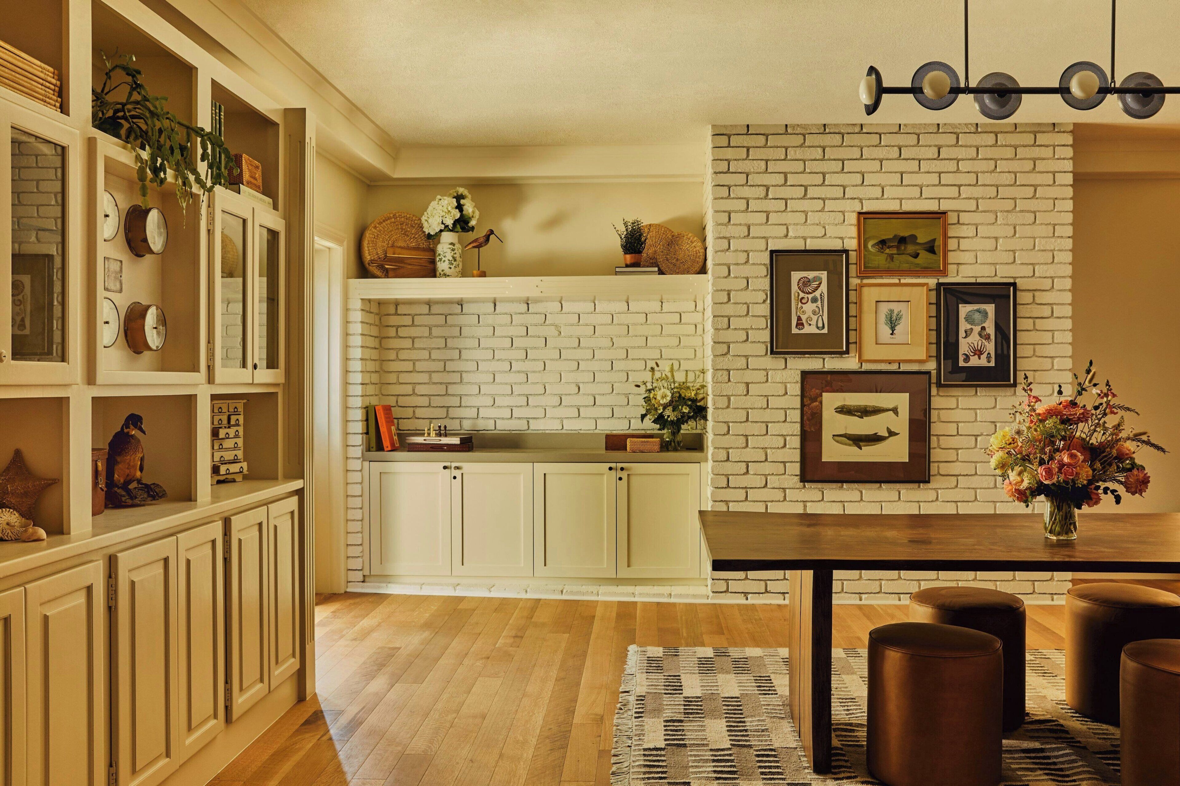 A modern kitchen with white brick walls, wooden cabinets, and a dining area with a wooden table and leather ottomans.